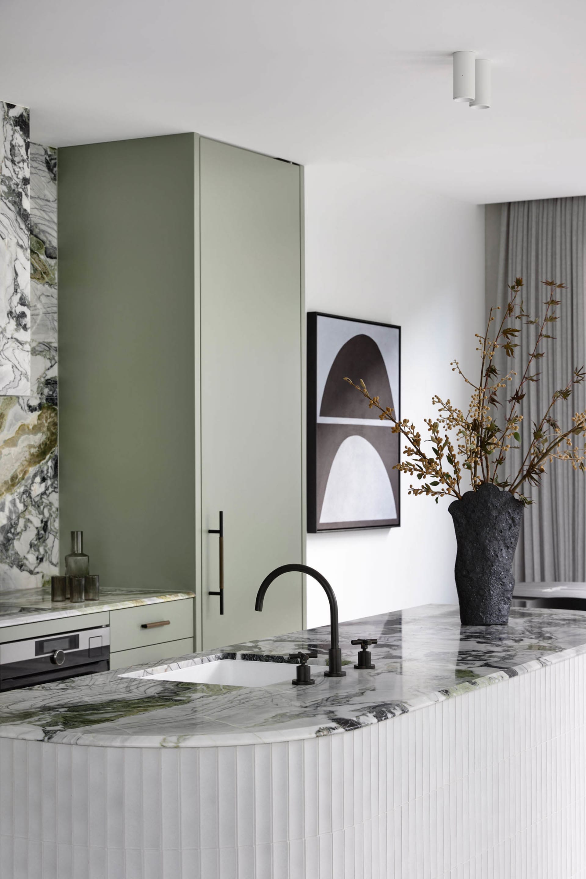 A modern minimalist kitchen features a white and green marble countertop, with a black faucet and contemporary green cabinetr