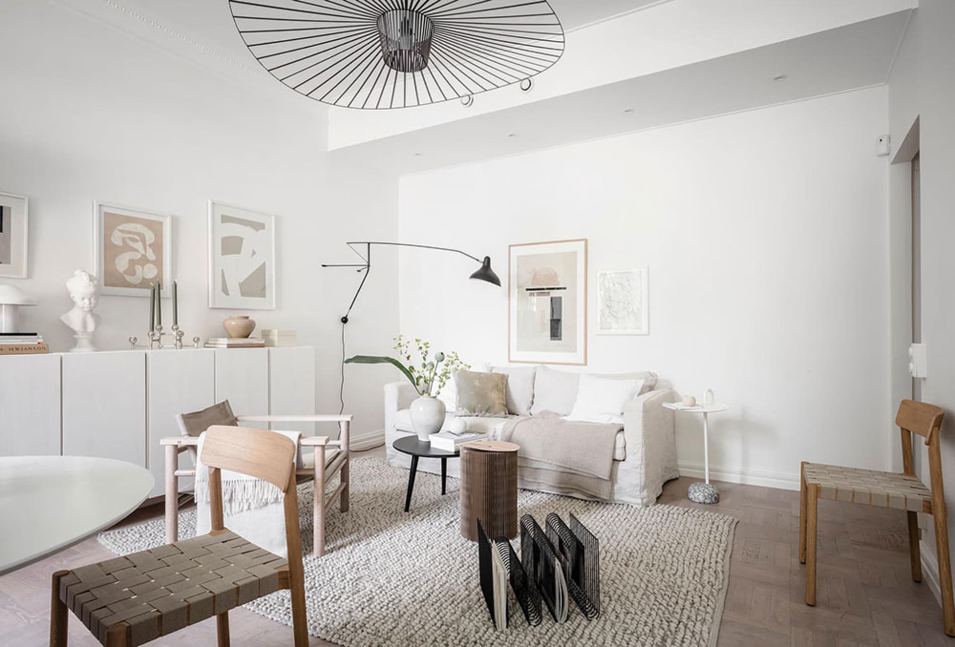 A modern minimalist living room with neutral-toned furniture and decor, featuring a white sofa, wooden chairs, and a black an