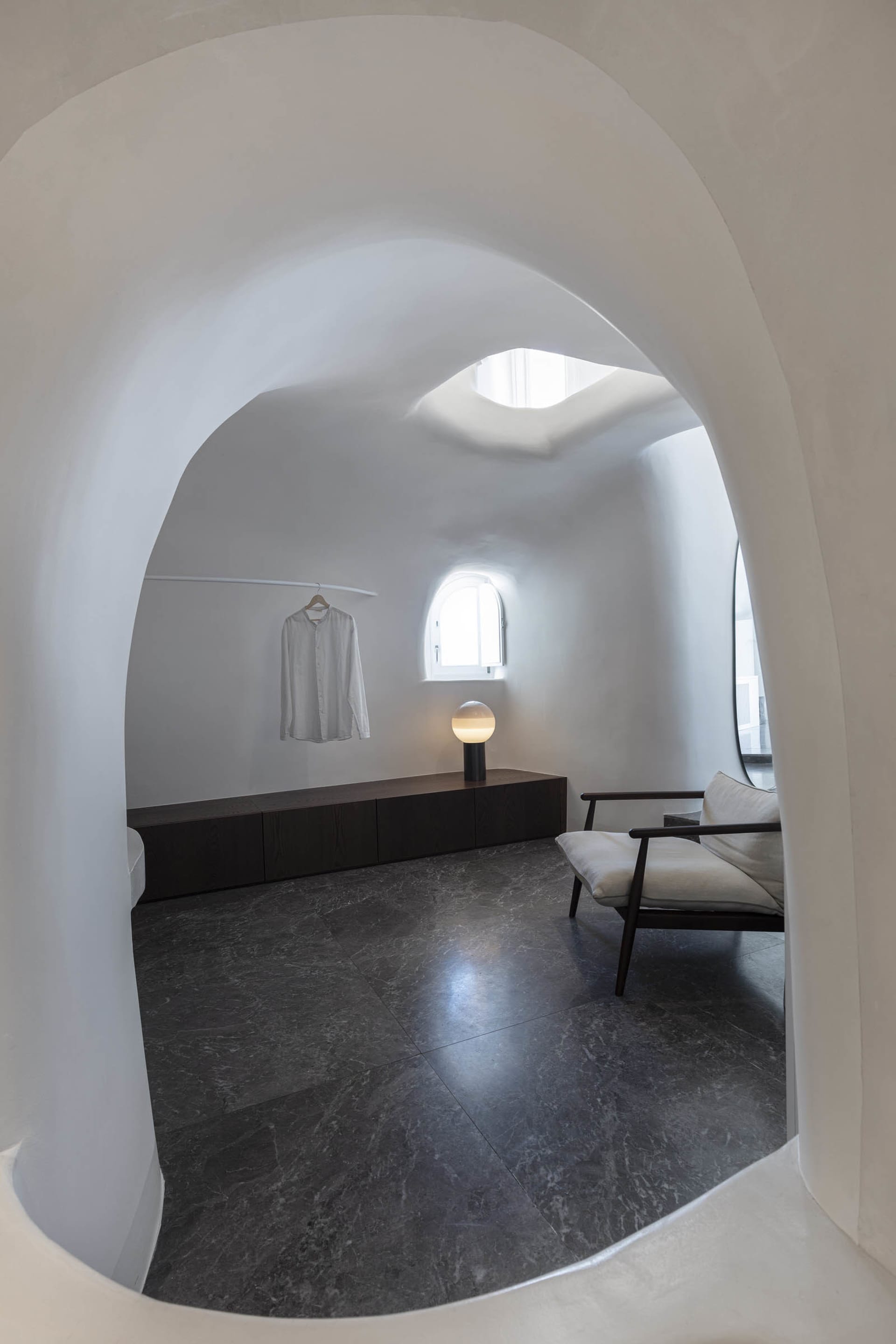 A modern, minimalist residential interior with white cement walls, dark marble floor, and a minimalist seating area with a wh
