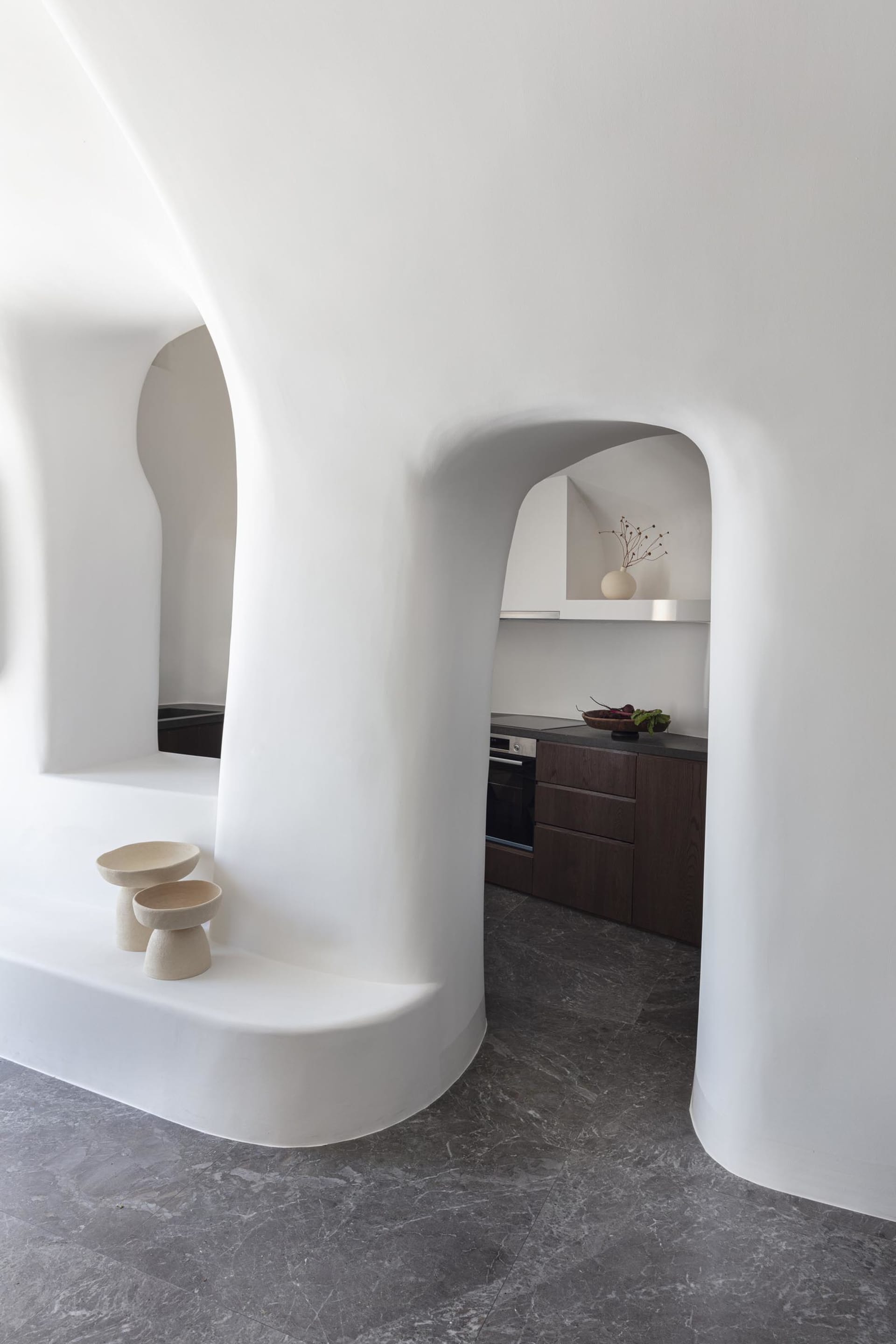 A modern, minimalist kitchen with white curved walls and marble countertops, featuring dark wood cabinets and a sleek, contem