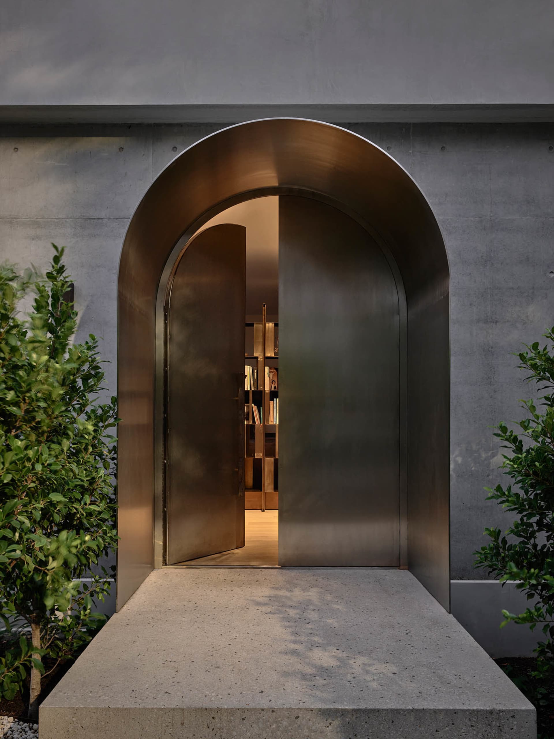 An arched, metallic entrance with a concrete base, leading to a warmly lit interior.
