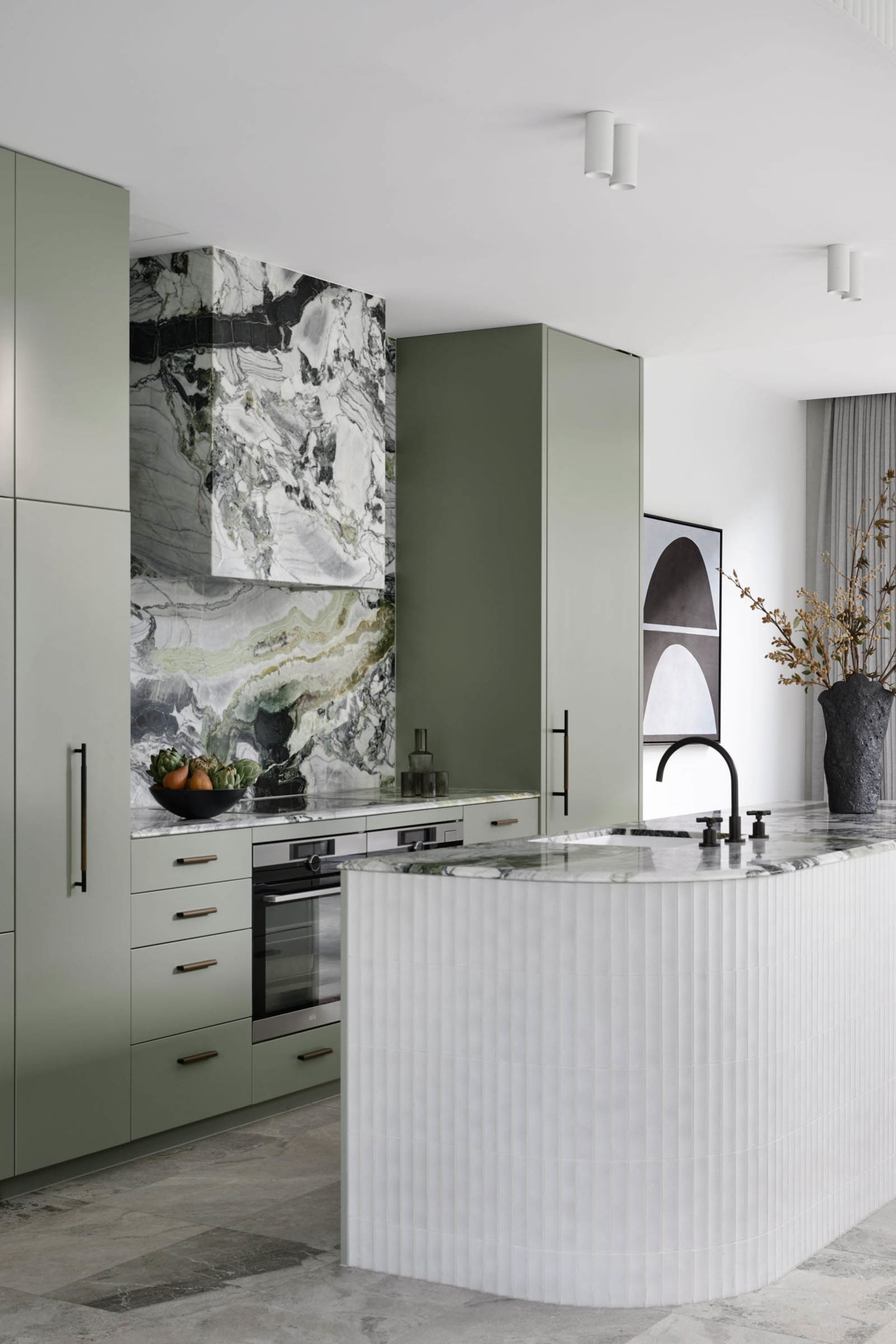 A sleek, minimalist kitchen featuring marble countertops and backsplash, modern appliances, and a curved island.