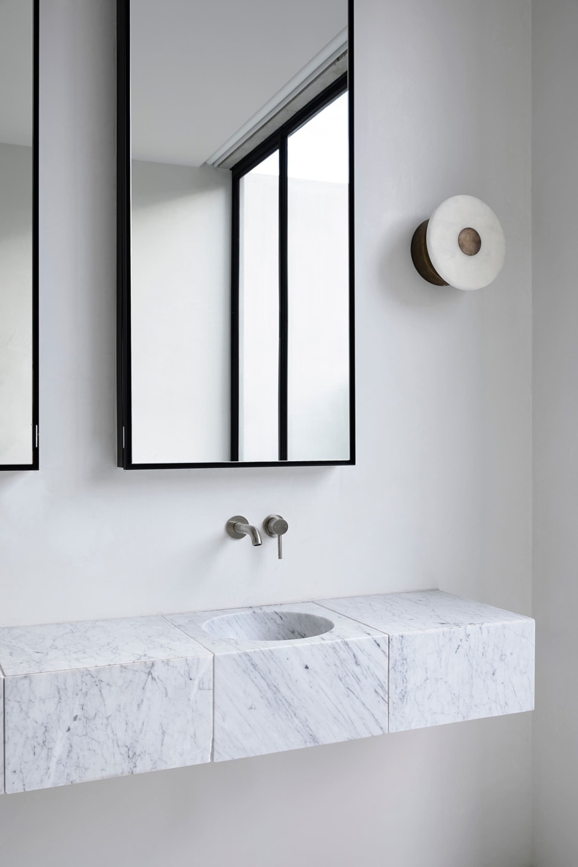A modern minimalist bathroom with a marble countertop and sink, a large mirror, and a window with a white frame.
