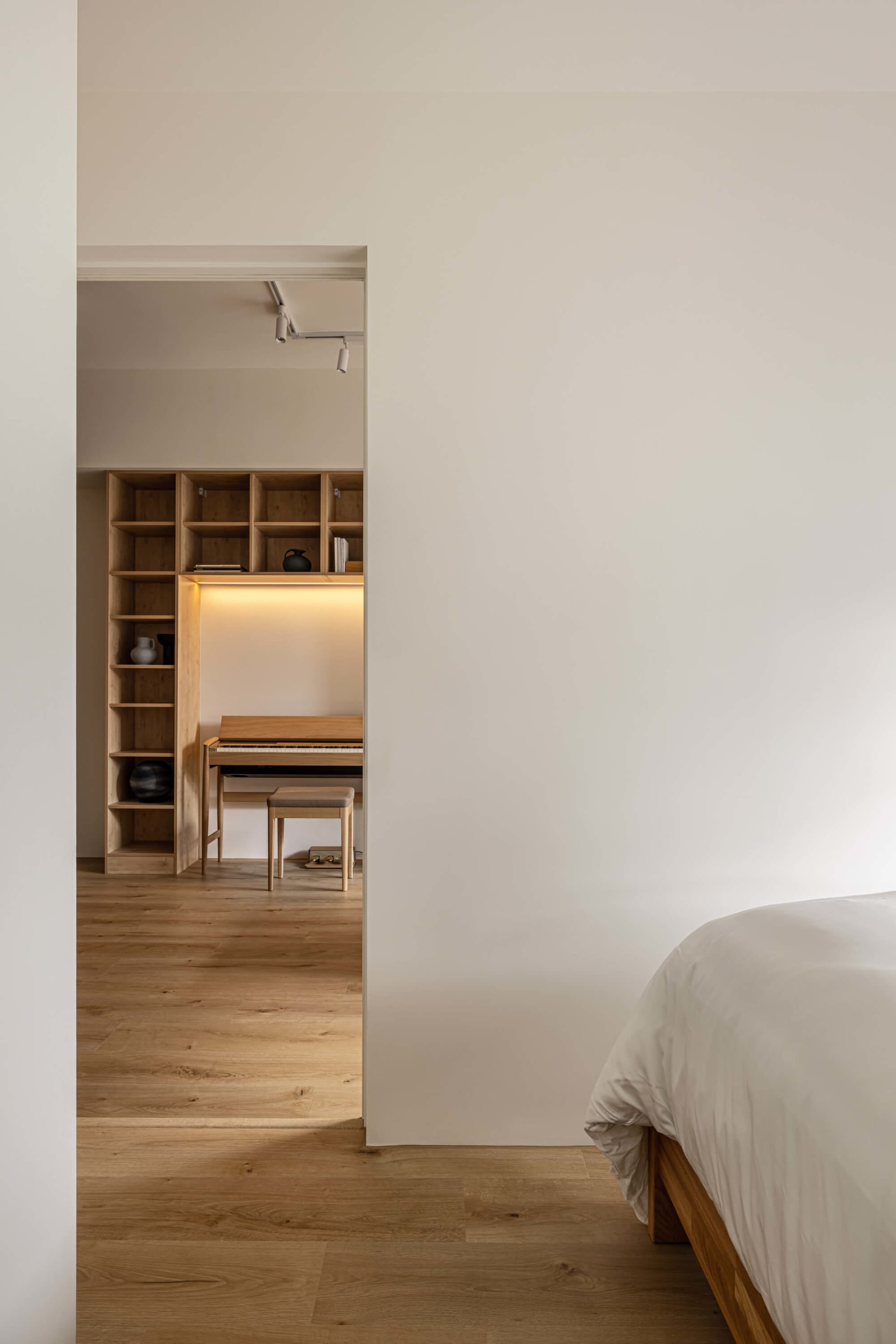A modern bedroom featuring a wooden bed against a white wall with a wooden shelving unit and a piano.