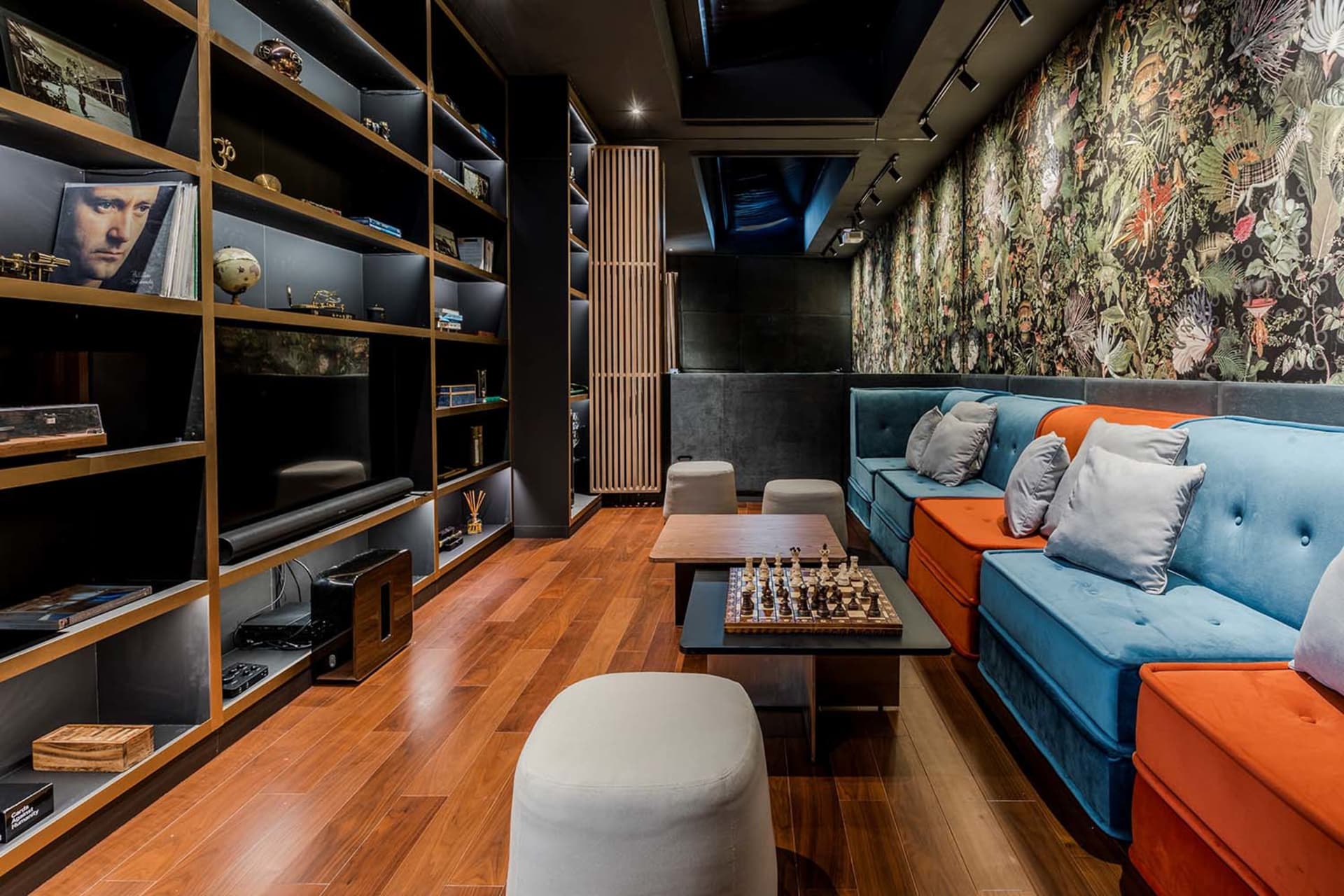 Modern industrial living room with blue and orange sofas, wooden floor, and bookshelves.