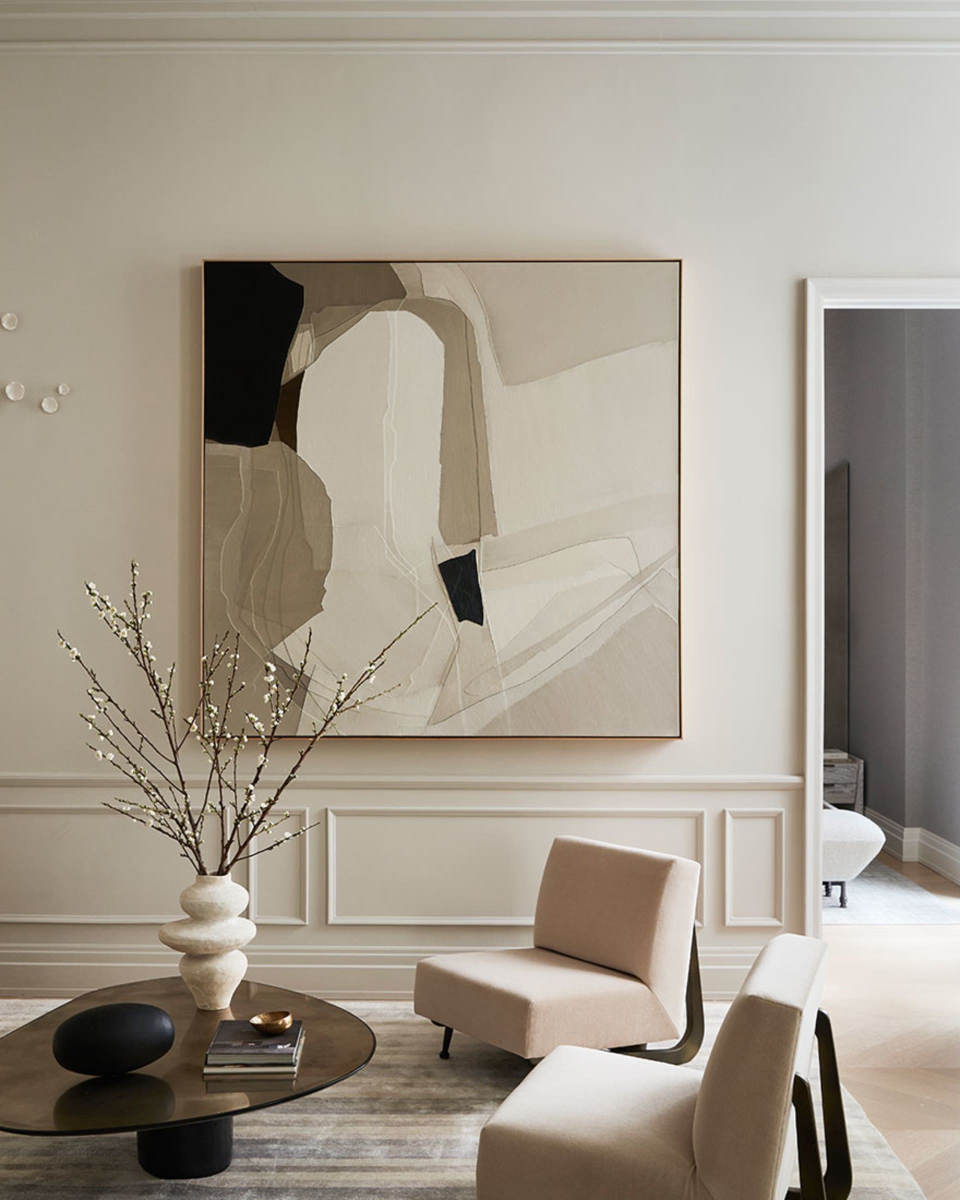 A modern living room with beige walls, minimalist furniture, and abstract artwork on the wall.