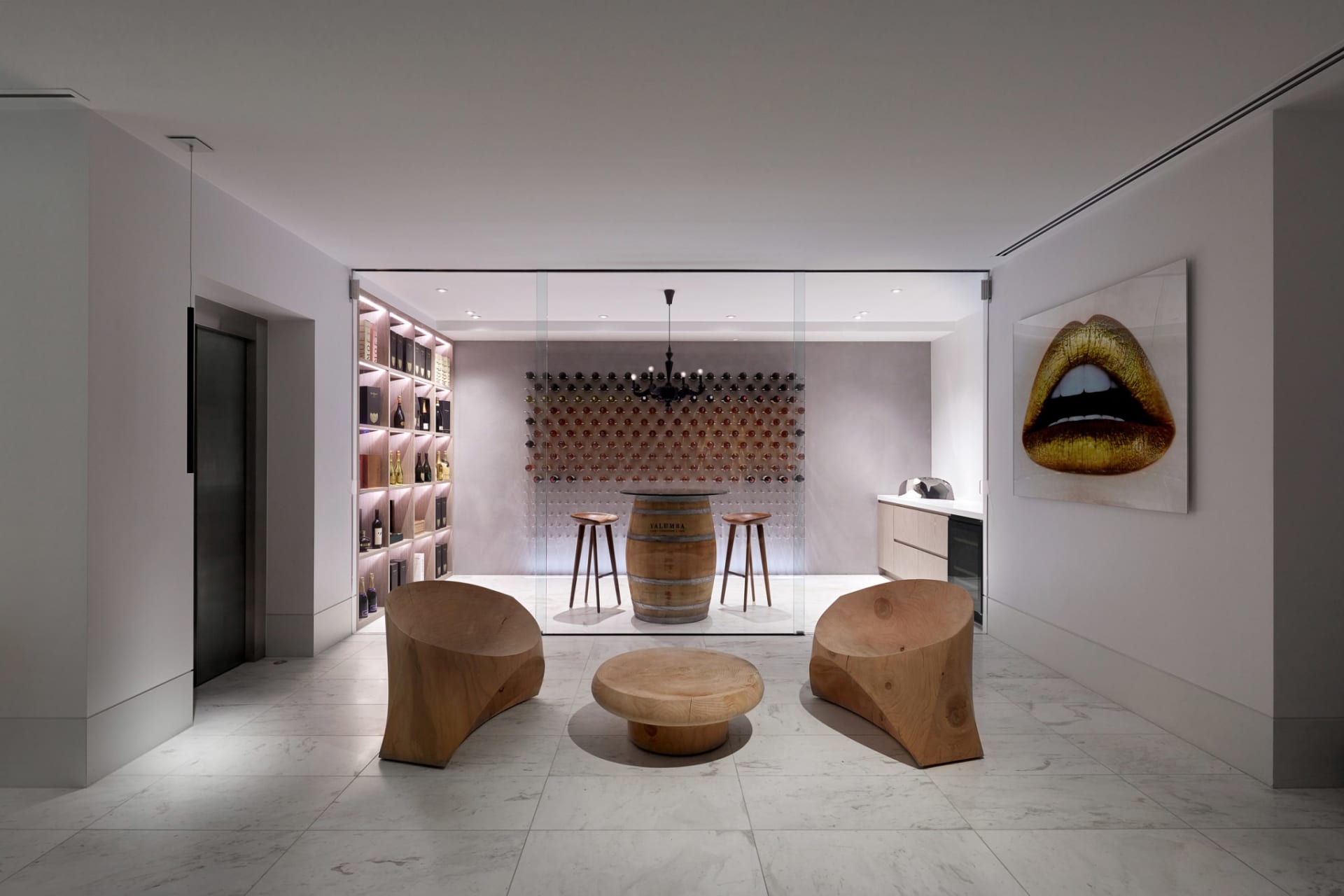 A modern wine tasting room featuring a barrel table, stools, wine bottles, and a large wine collection on the wall.