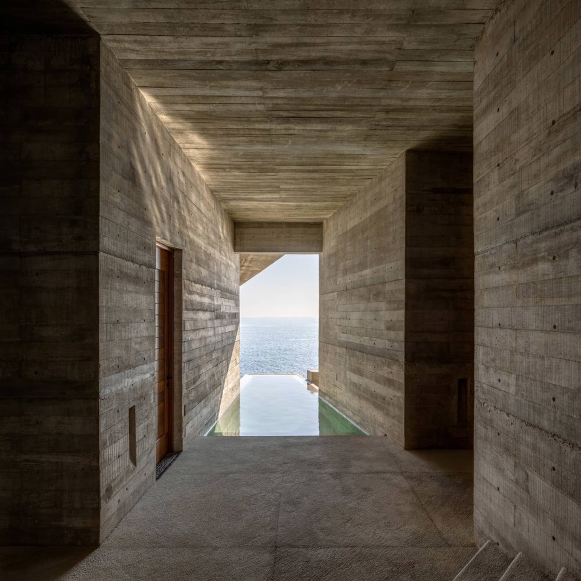 A modern interior with a concrete wall revealing a scenic ocean view.