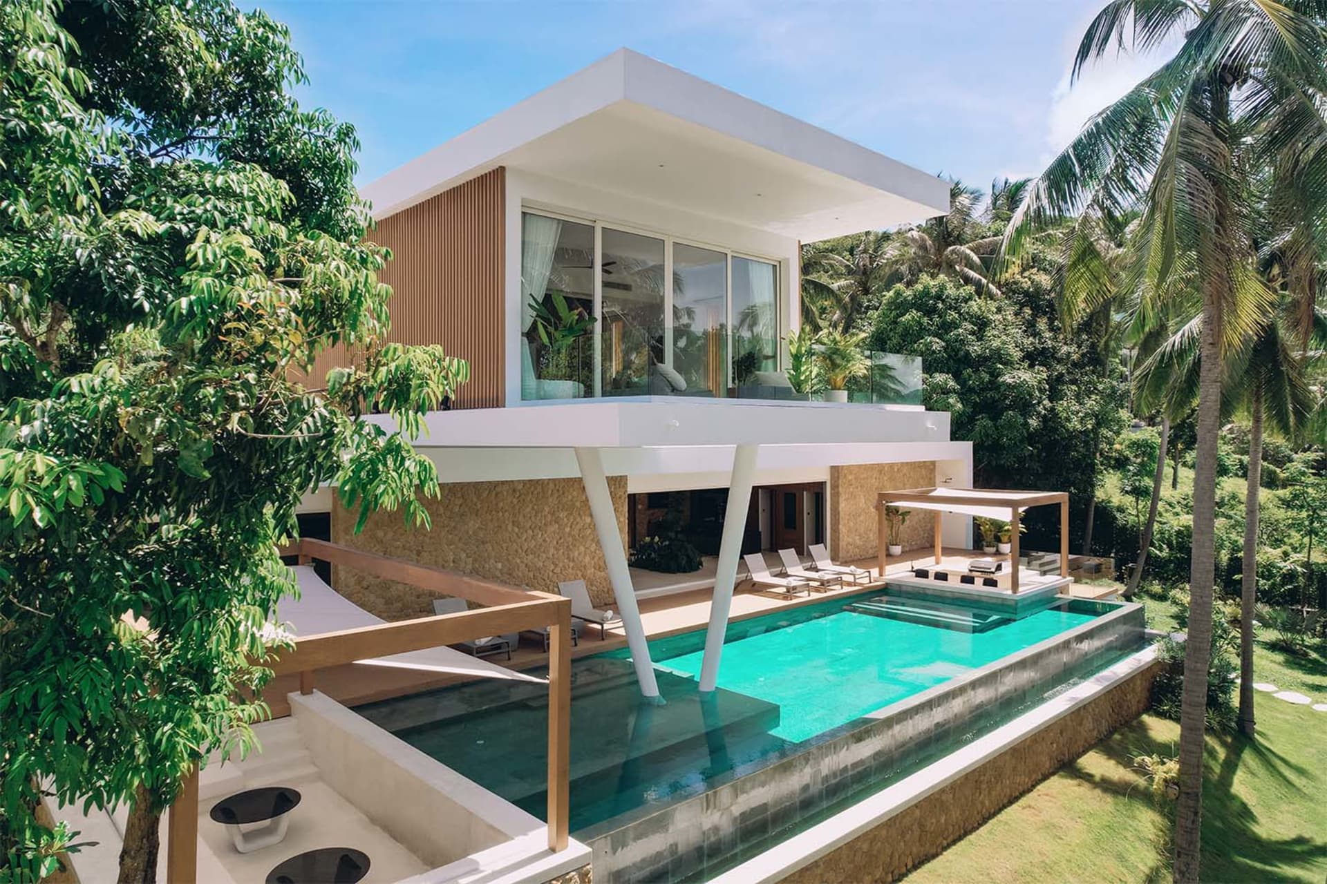 Modern residential villa with a swimming pool surrounded by palm trees, featuring glass and concrete exterior walls and woode