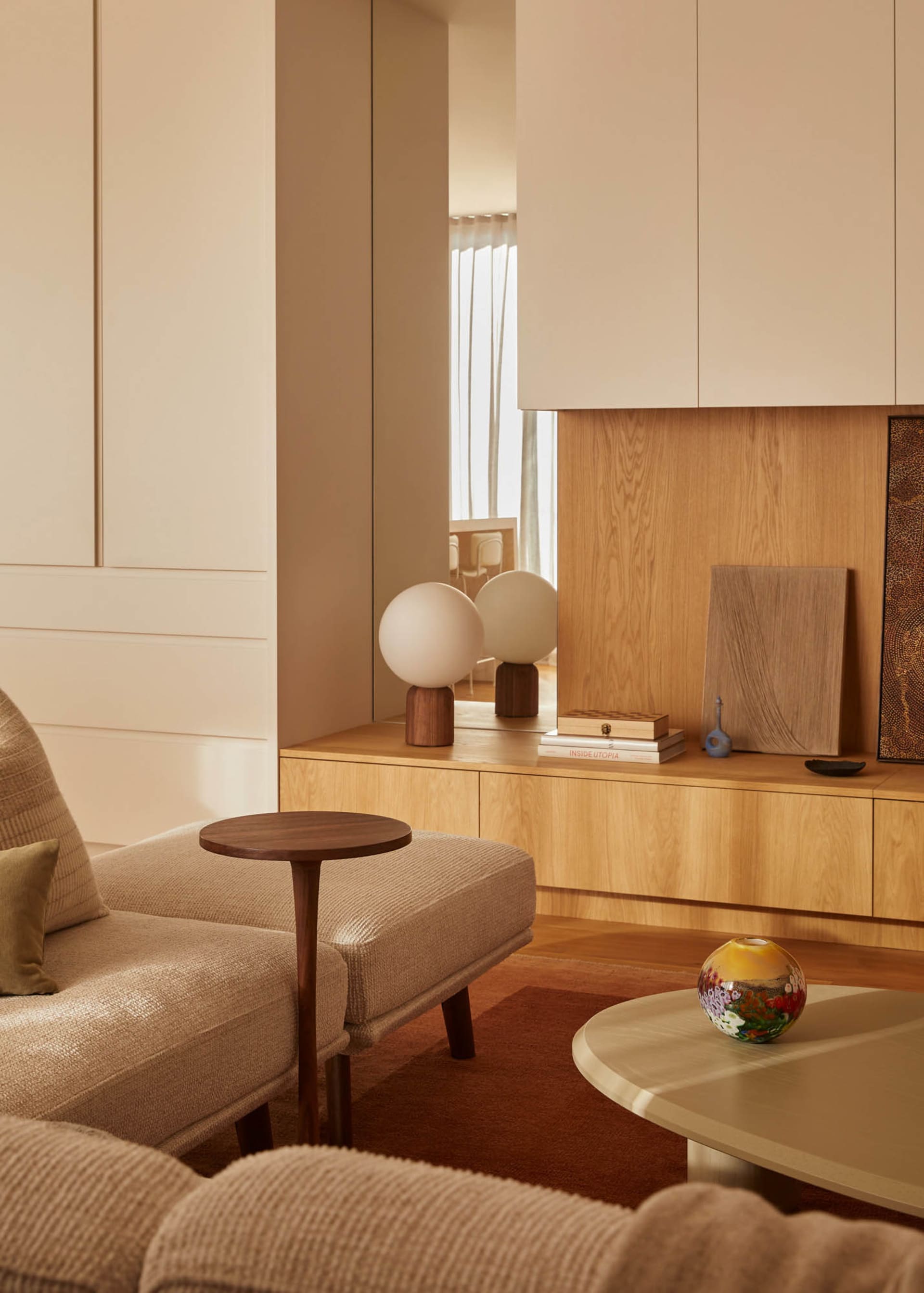 Modern, minimalist living room with wooden cabinets, spherical lamps, and neutral-toned furniture.