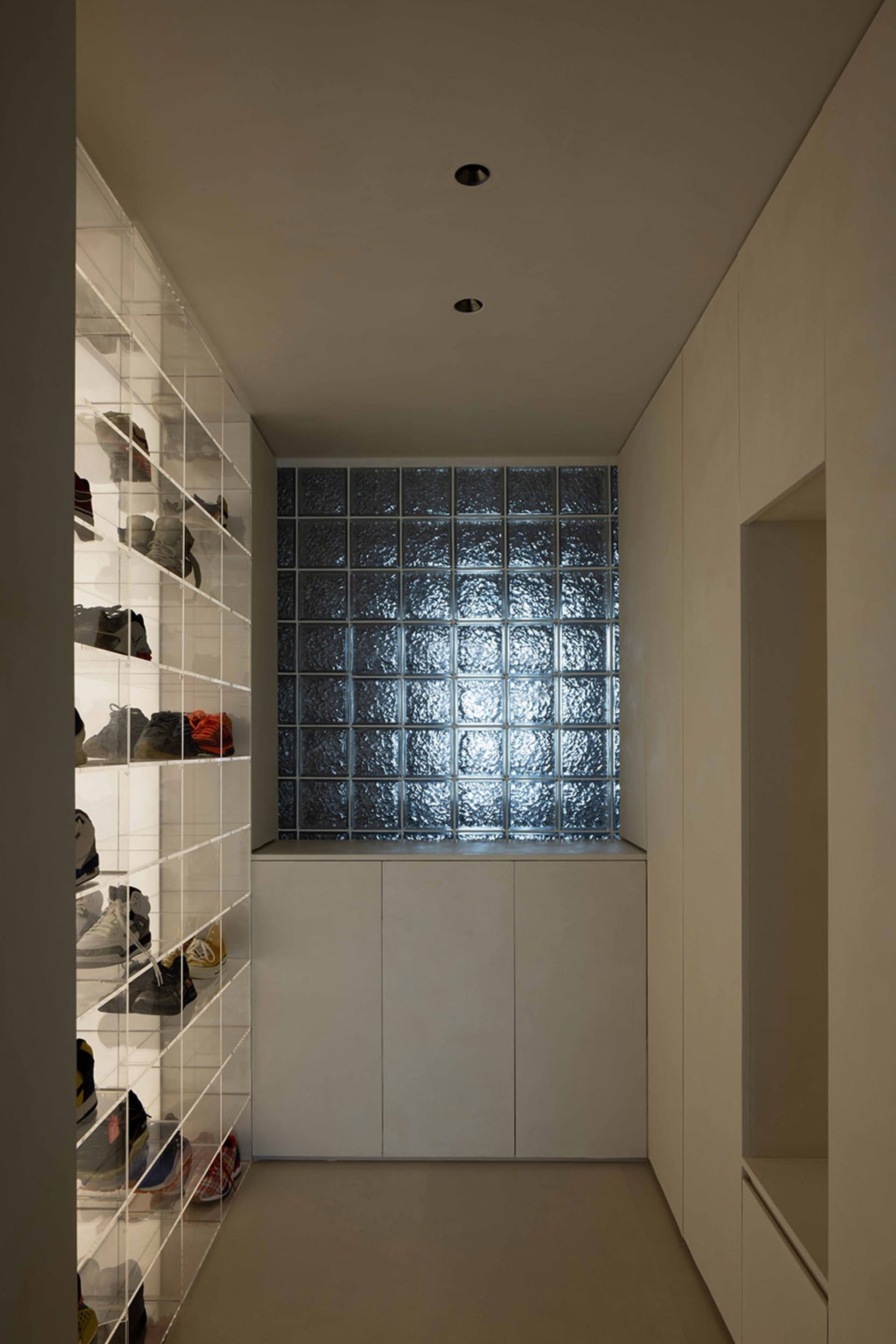 A minimalist shoe closet featuring a glass wall and storage units