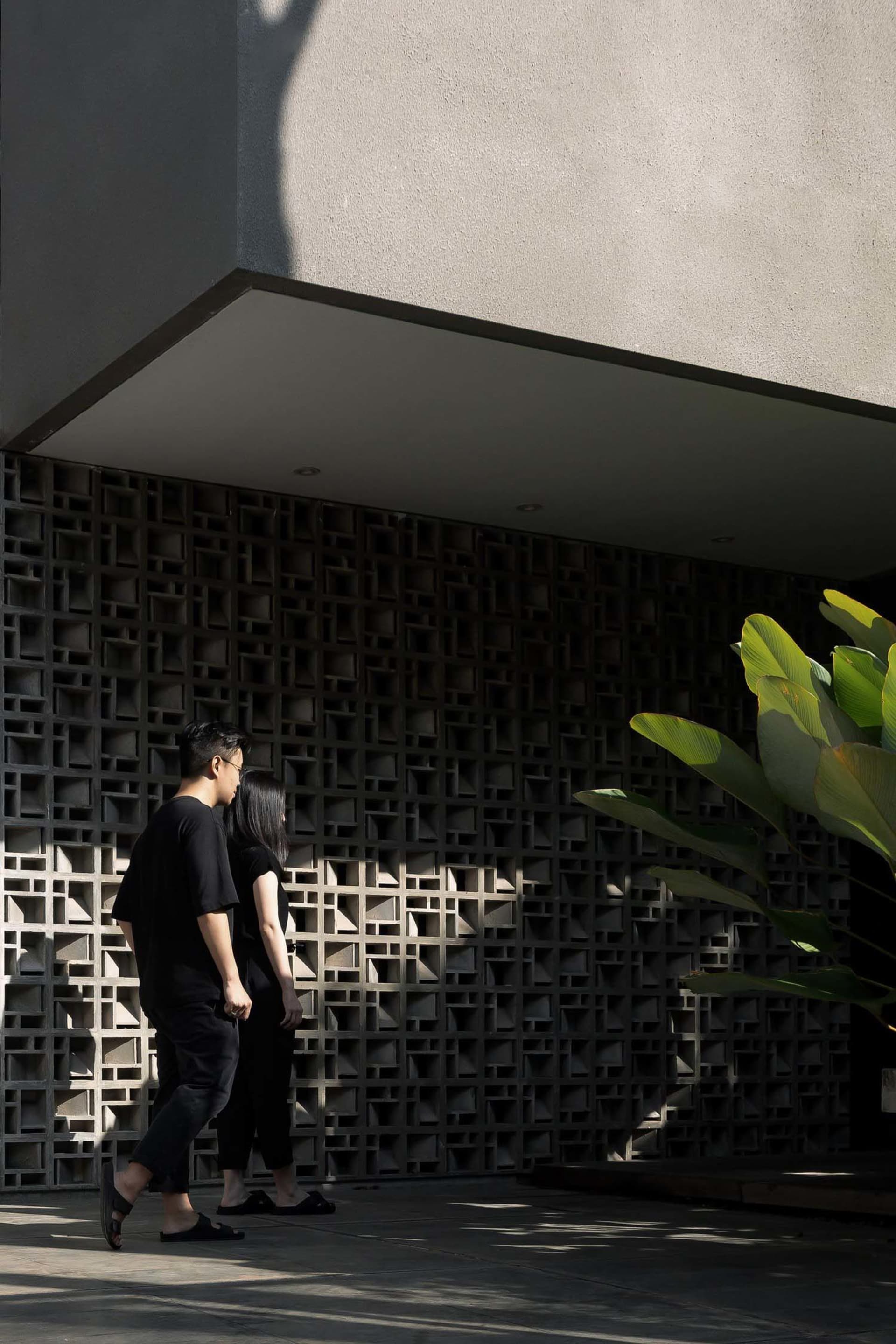 兩人走過一棟現代黑白建築,格柵牆面與前景綠意相映