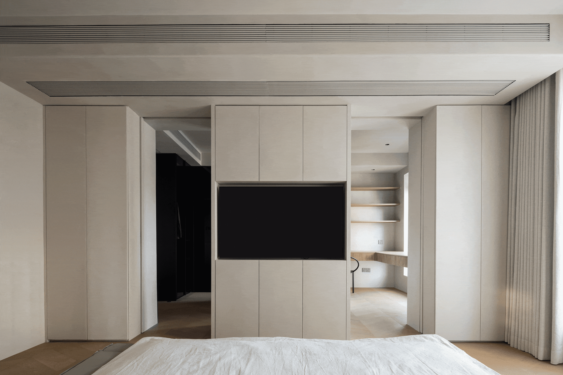 Modern minimalist bedroom with neutral-toned walls, built-in storage, and a large bed.