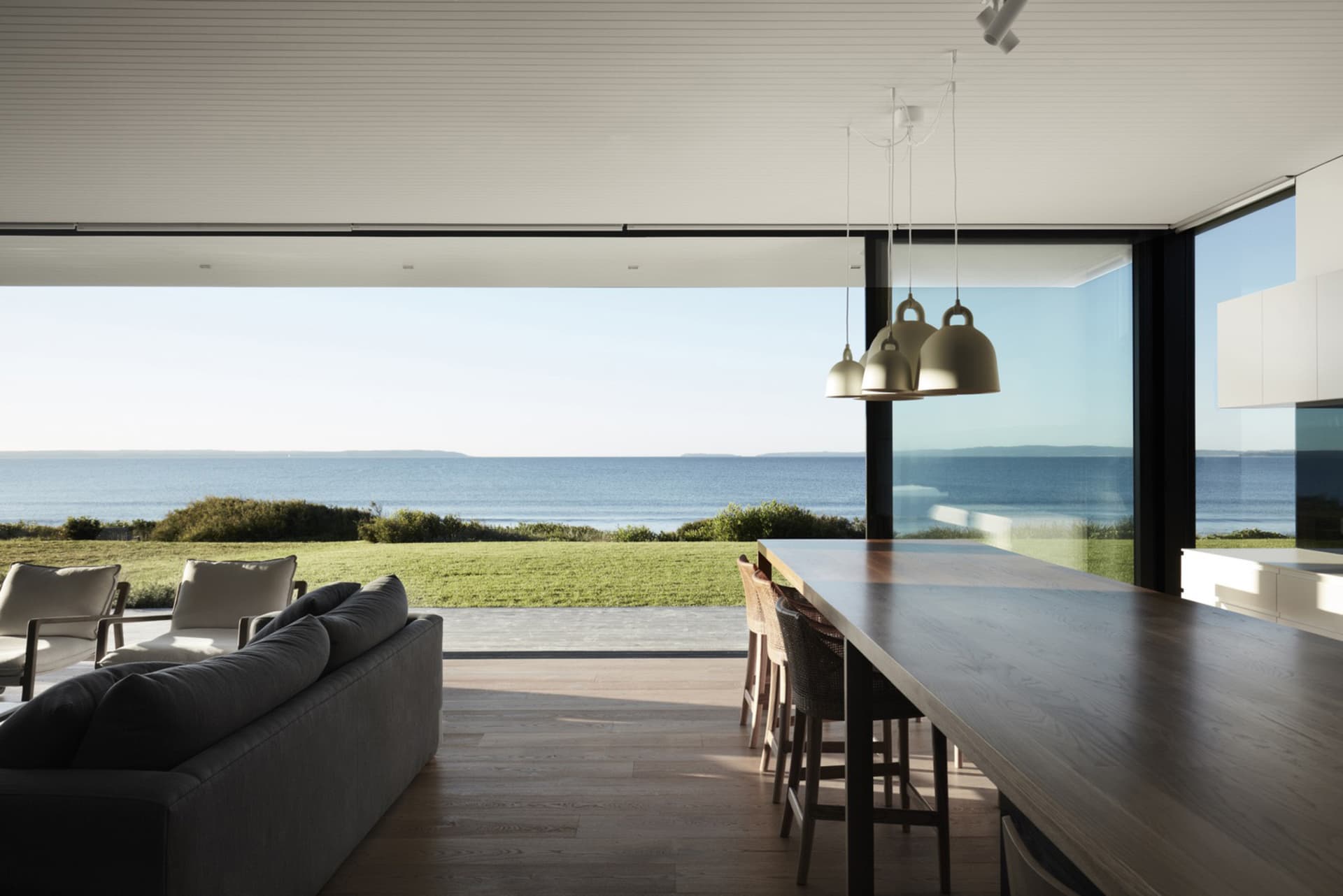 A modern living space featuring wood flooring, large glass windows, and a sleek metal dining table.