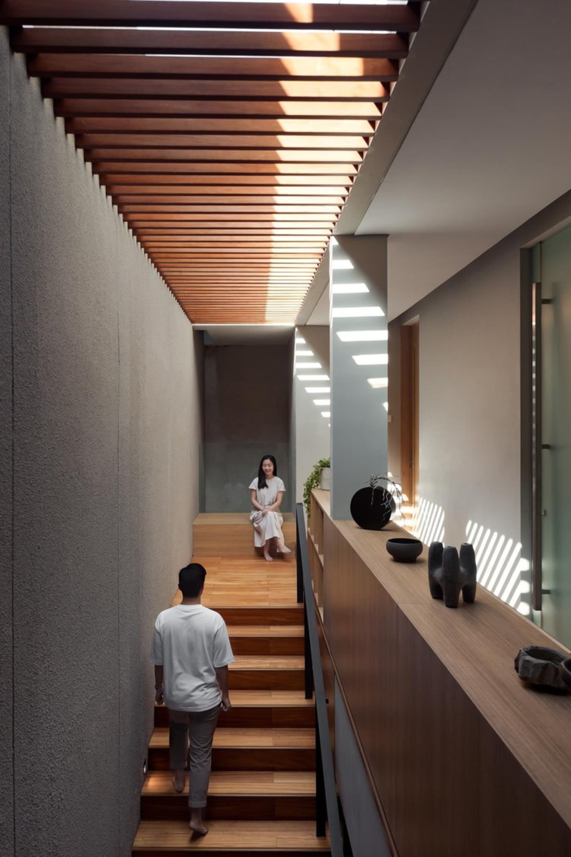 A modern minimalist hallway with wooden stairs and flooring, featuring a woman sitting on the stairs.
