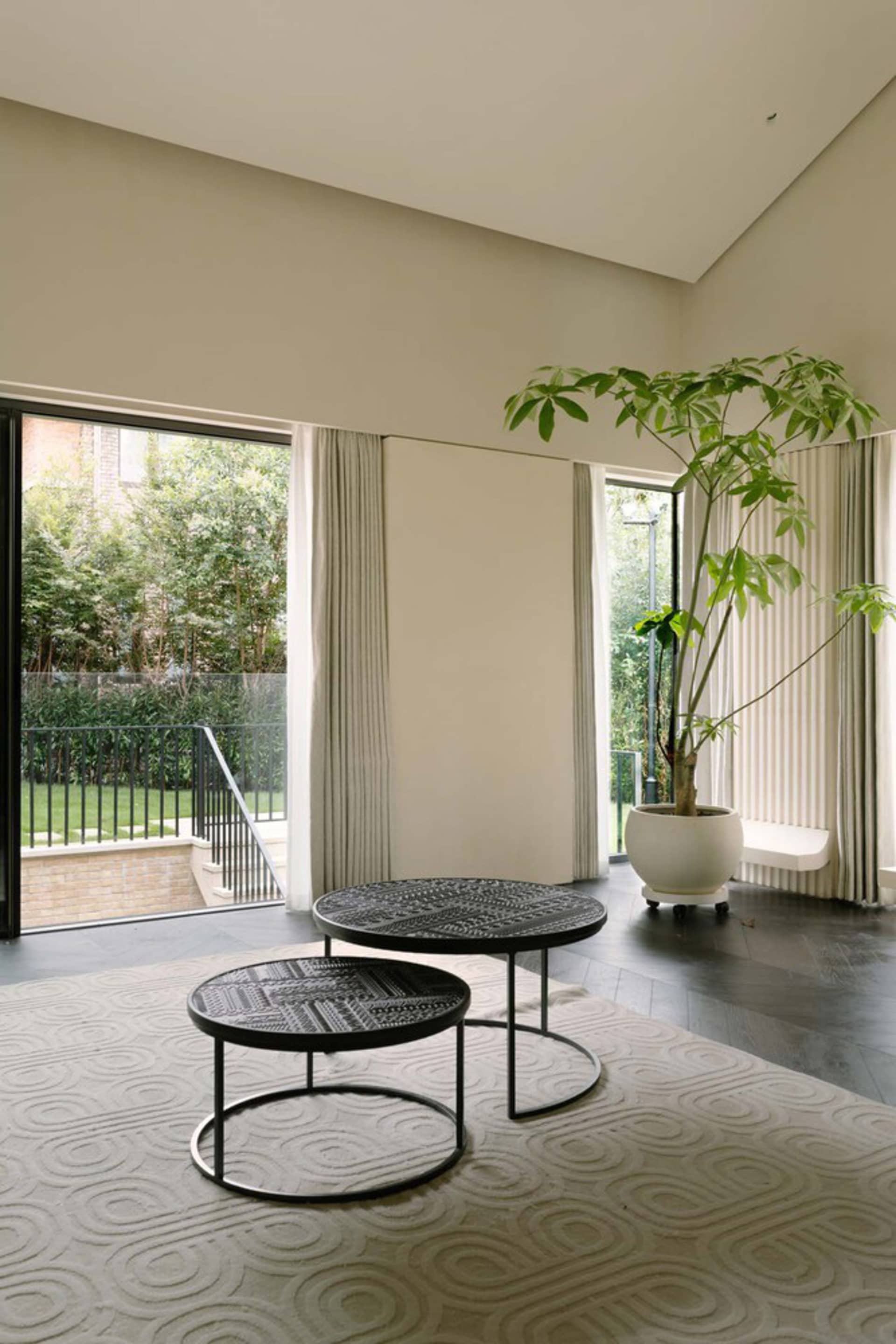 Modern living room featuring black metal coffee tables topped with cotton-covered cushions, with a tall green plant and floor