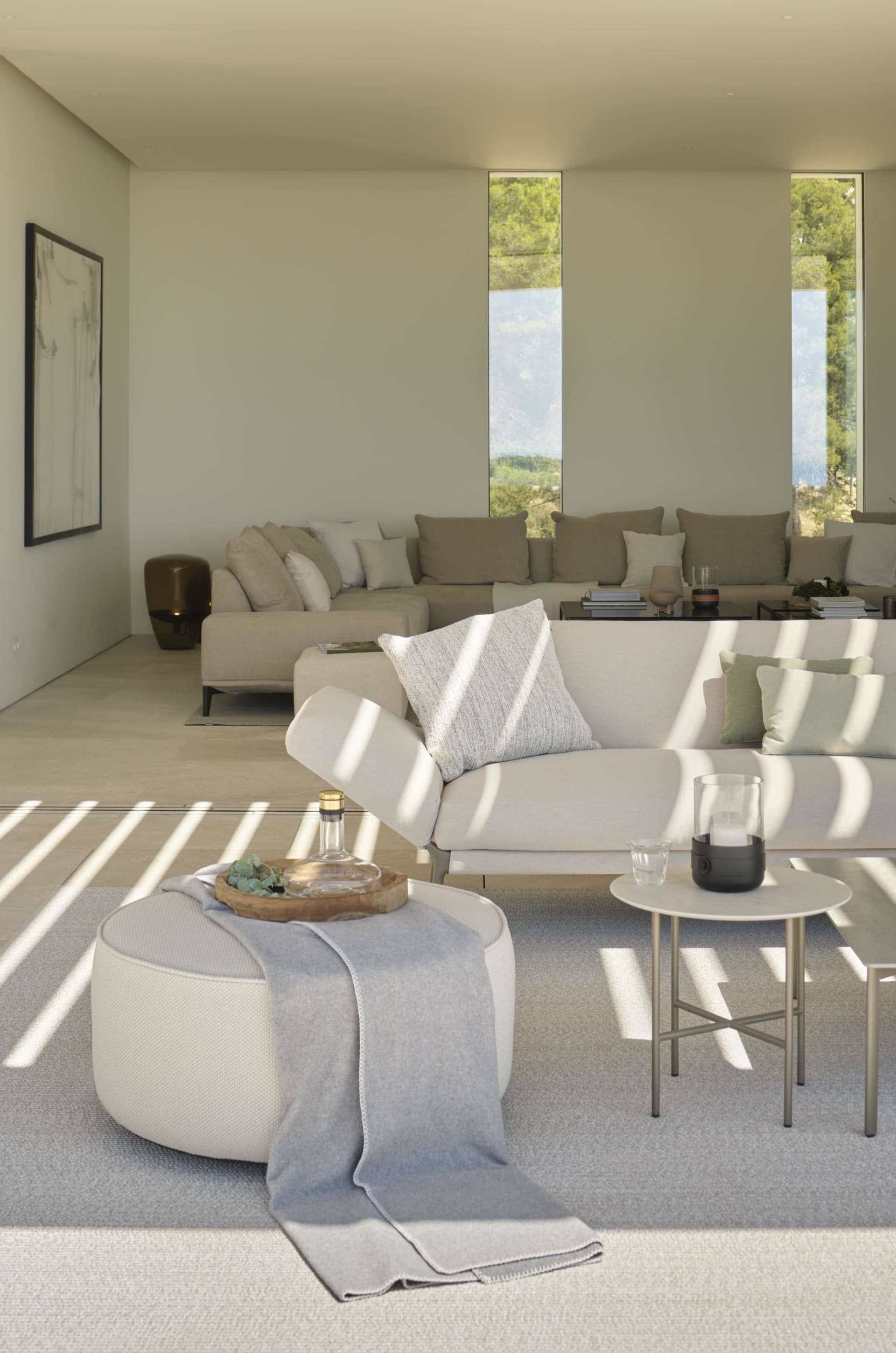 A minimalist living room featuring fabric sofas, glass coffee tables, and concrete flooring and walls.