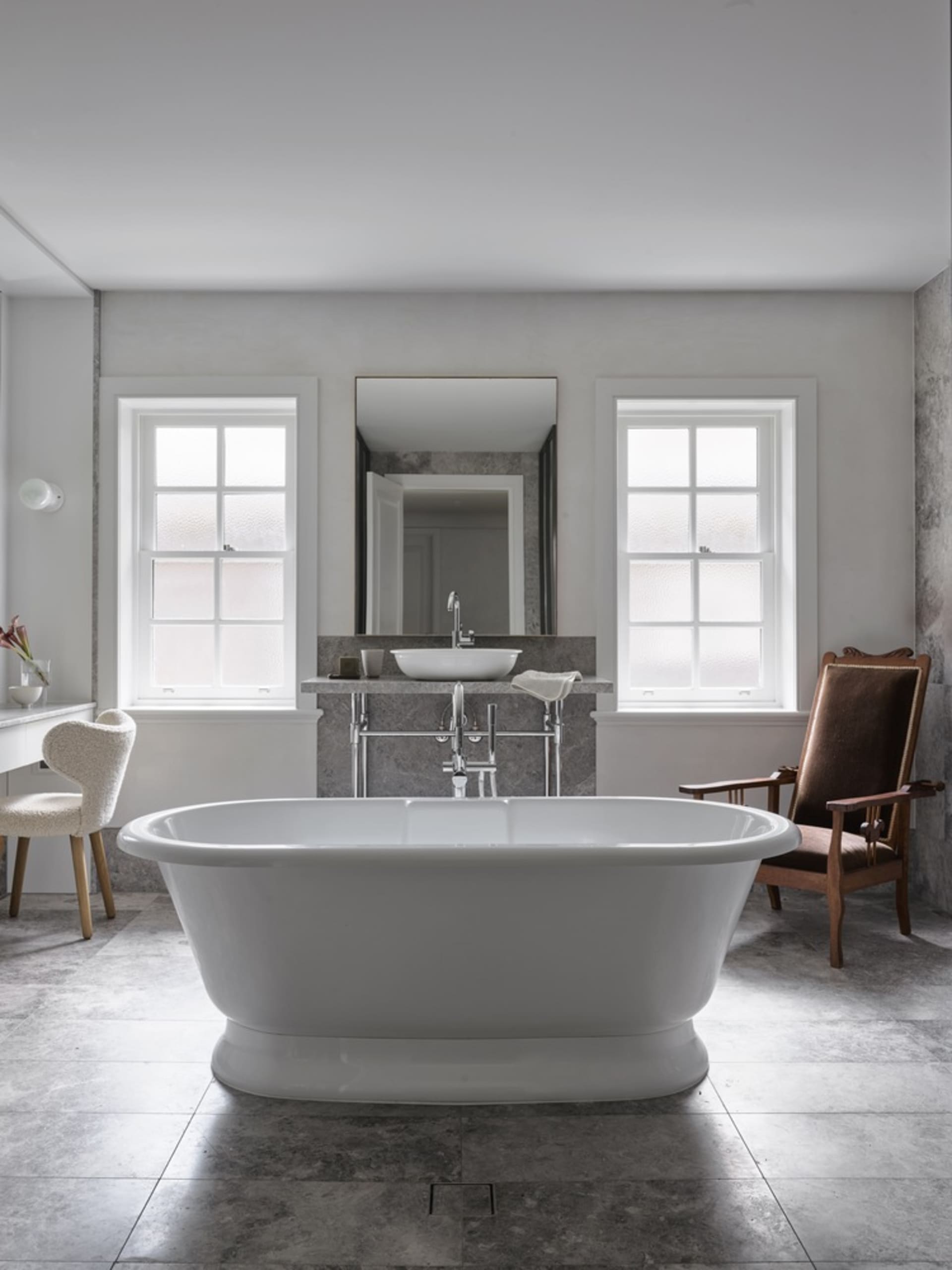 Modern bathroom interior with marble bathtub, sink, and chairs.
