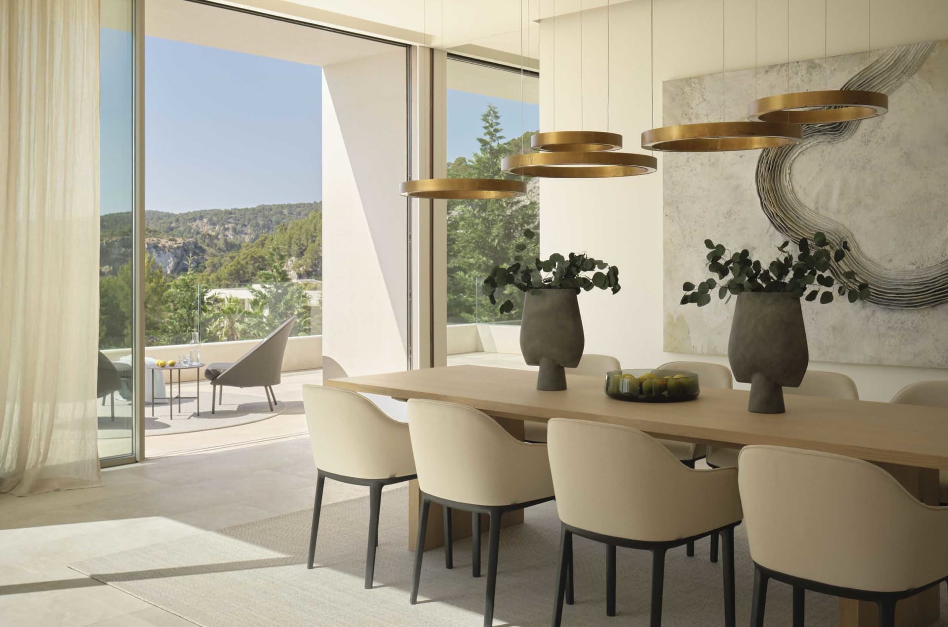 Modern dining room featuring marble and wooden elements, with gold pendant lights and a view of the outdoors.