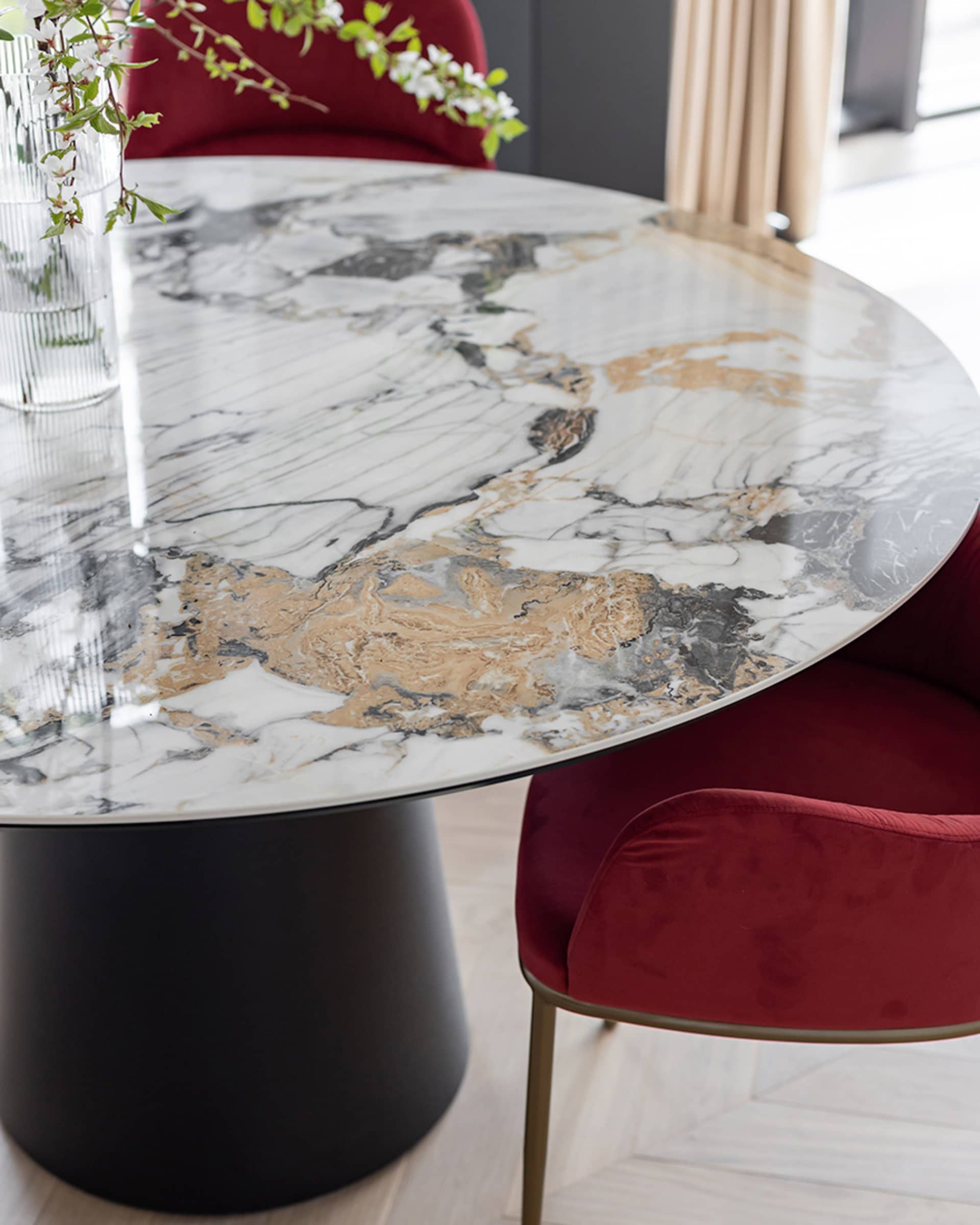 A modern dining room featuring a round marble table with a black base and red upholstered chairs.