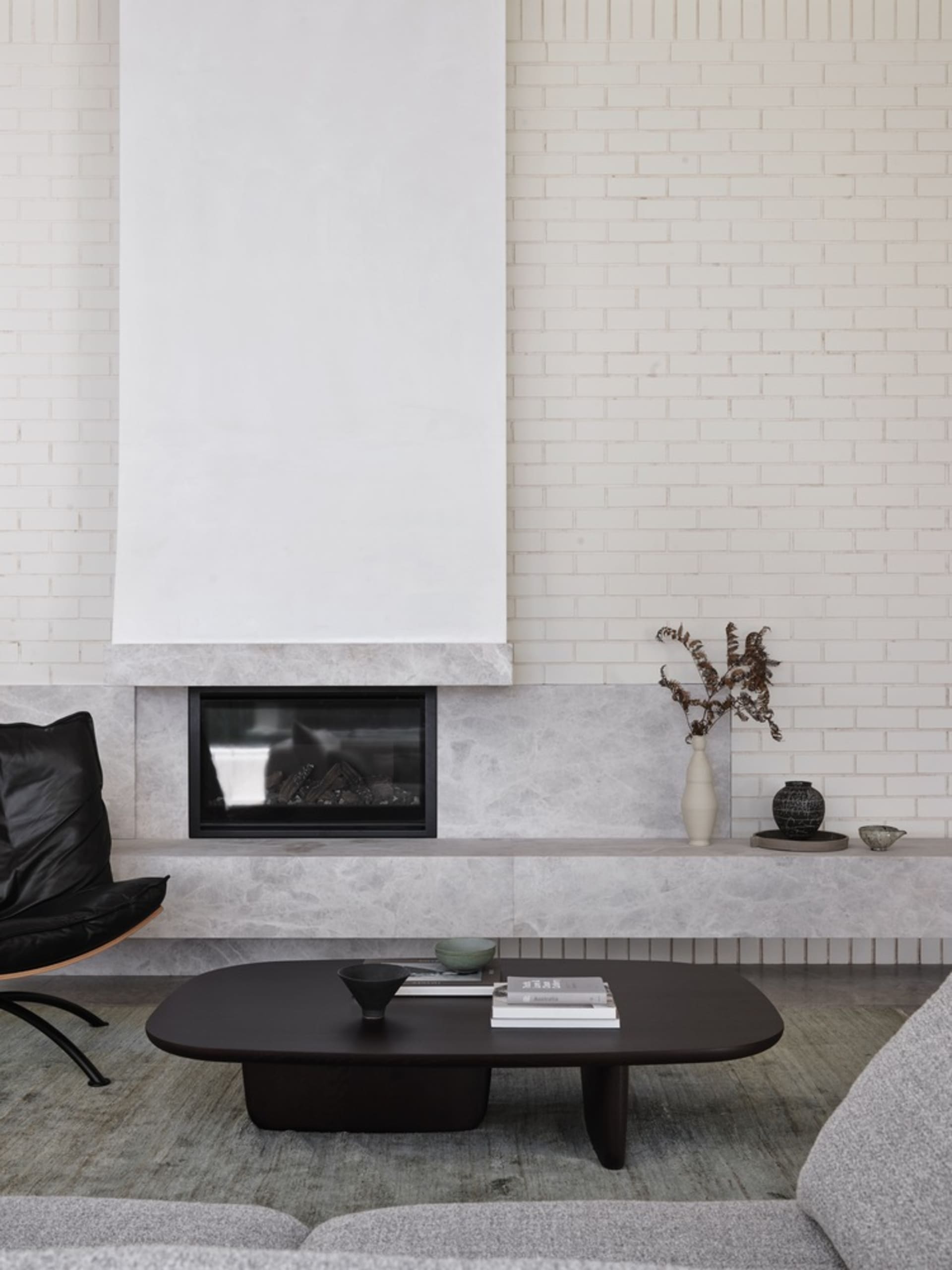 A modern living room featuring a grey marble fireplace and coffee table, with minimalist furniture and a white brick wall.