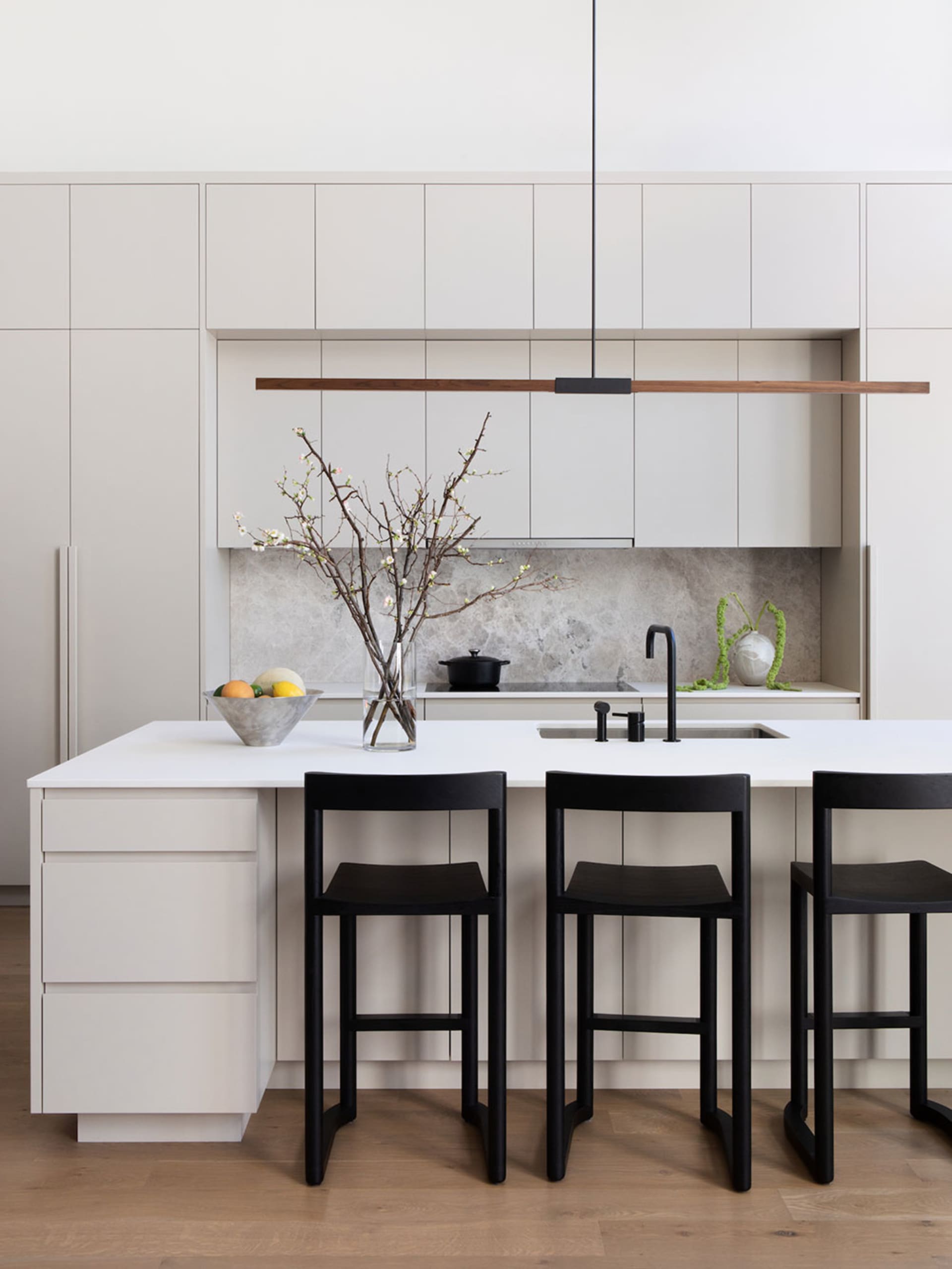 A minimalist kitchen with white cabinets, a white countertop, and black stools.