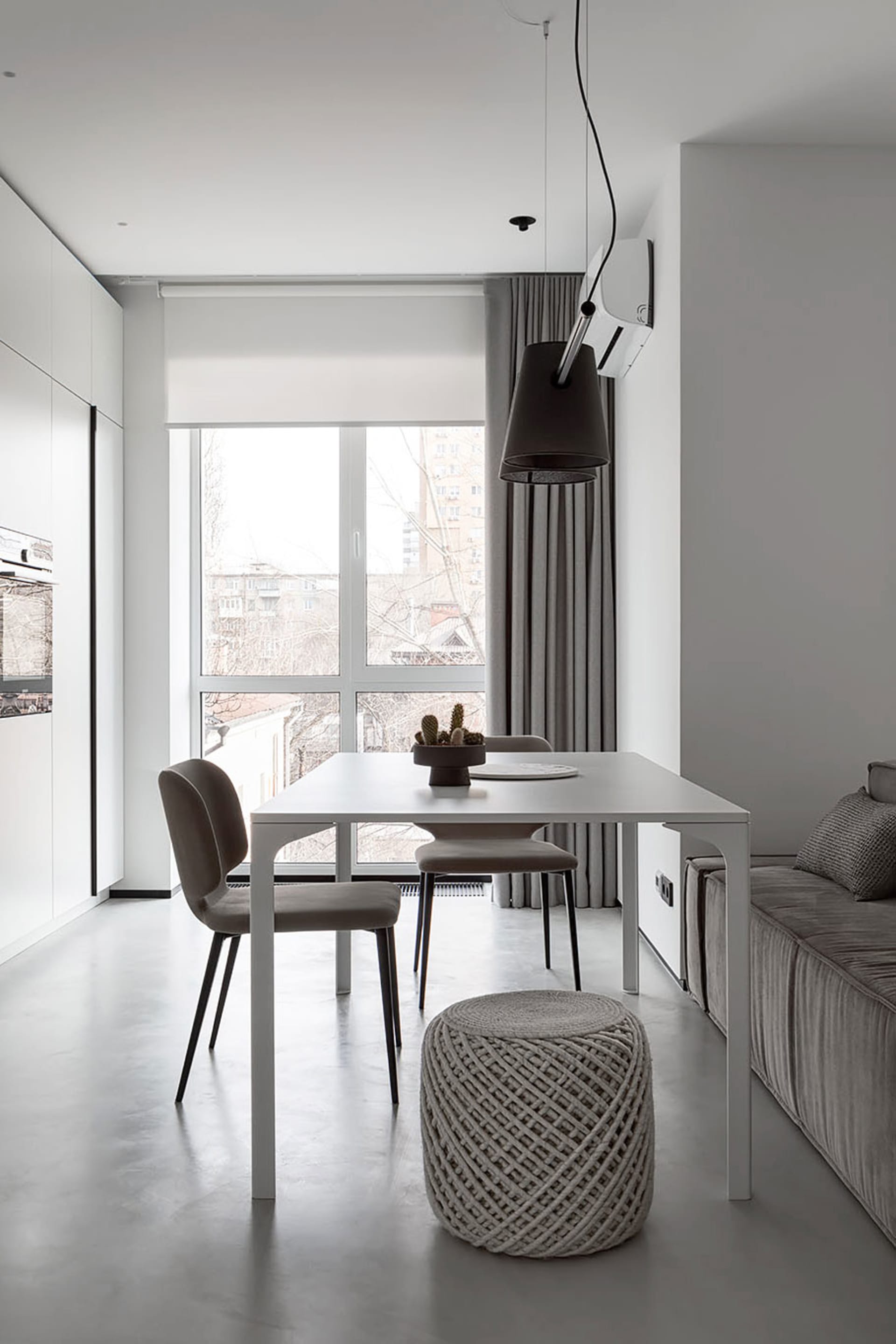 A modern minimalist living and dining room with a sleek white table and chairs, a large window, and a comfortable sofa.