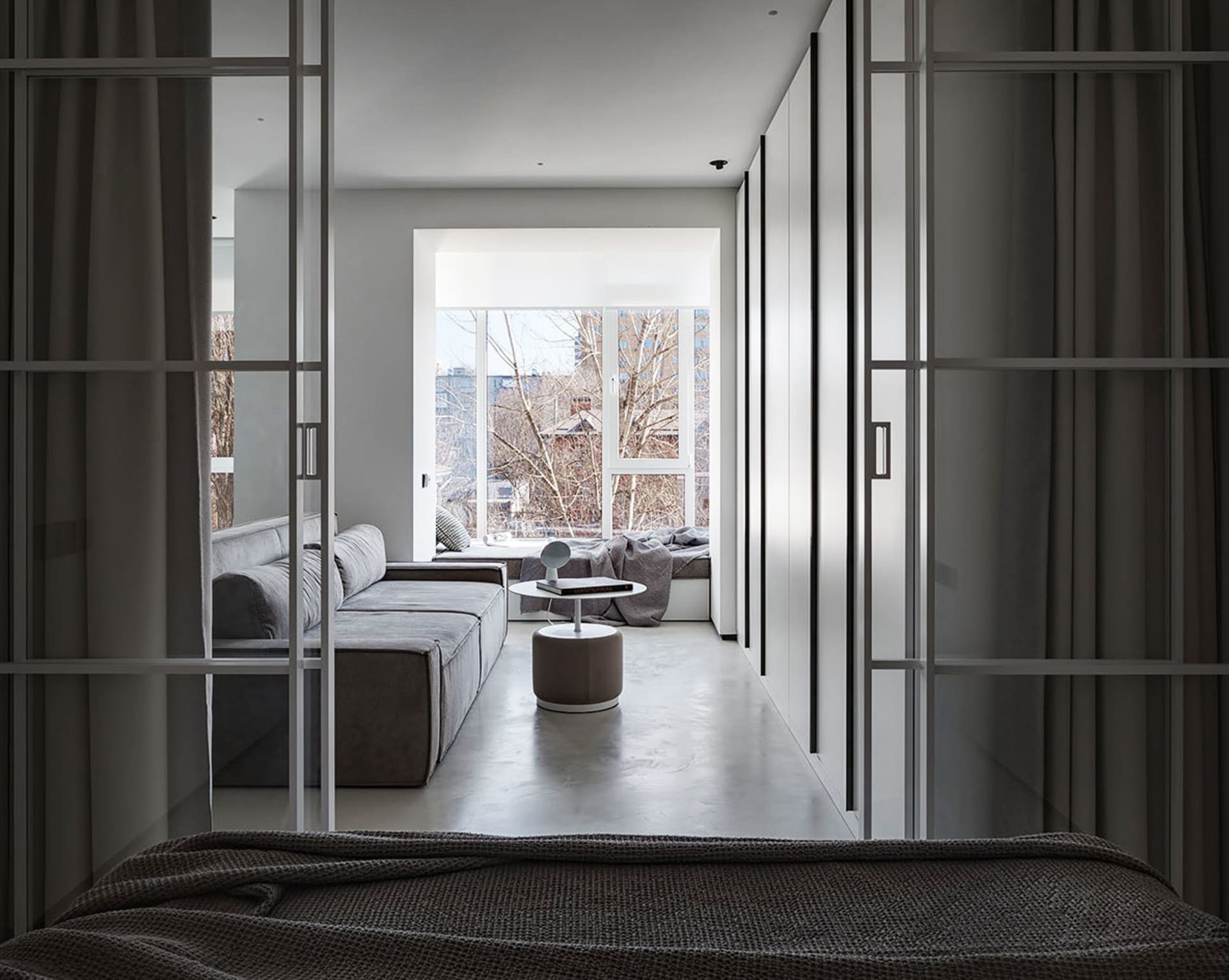 A modern living room featuring a concrete sectional sofa and a circular ottoman with a book on top.