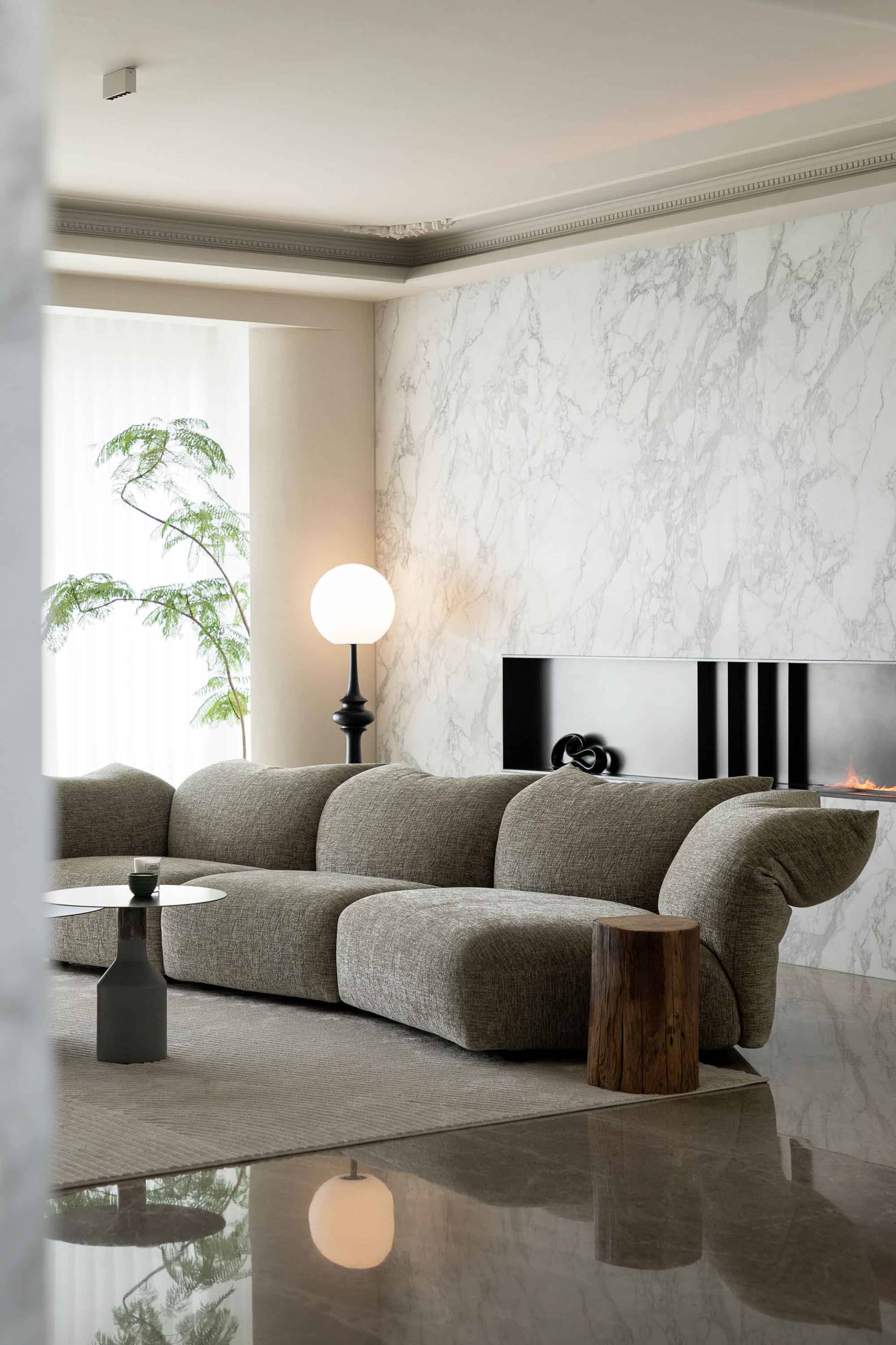 A contemporary living room featuring a modern sofa, marble fireplace wall, and minimalist decor.