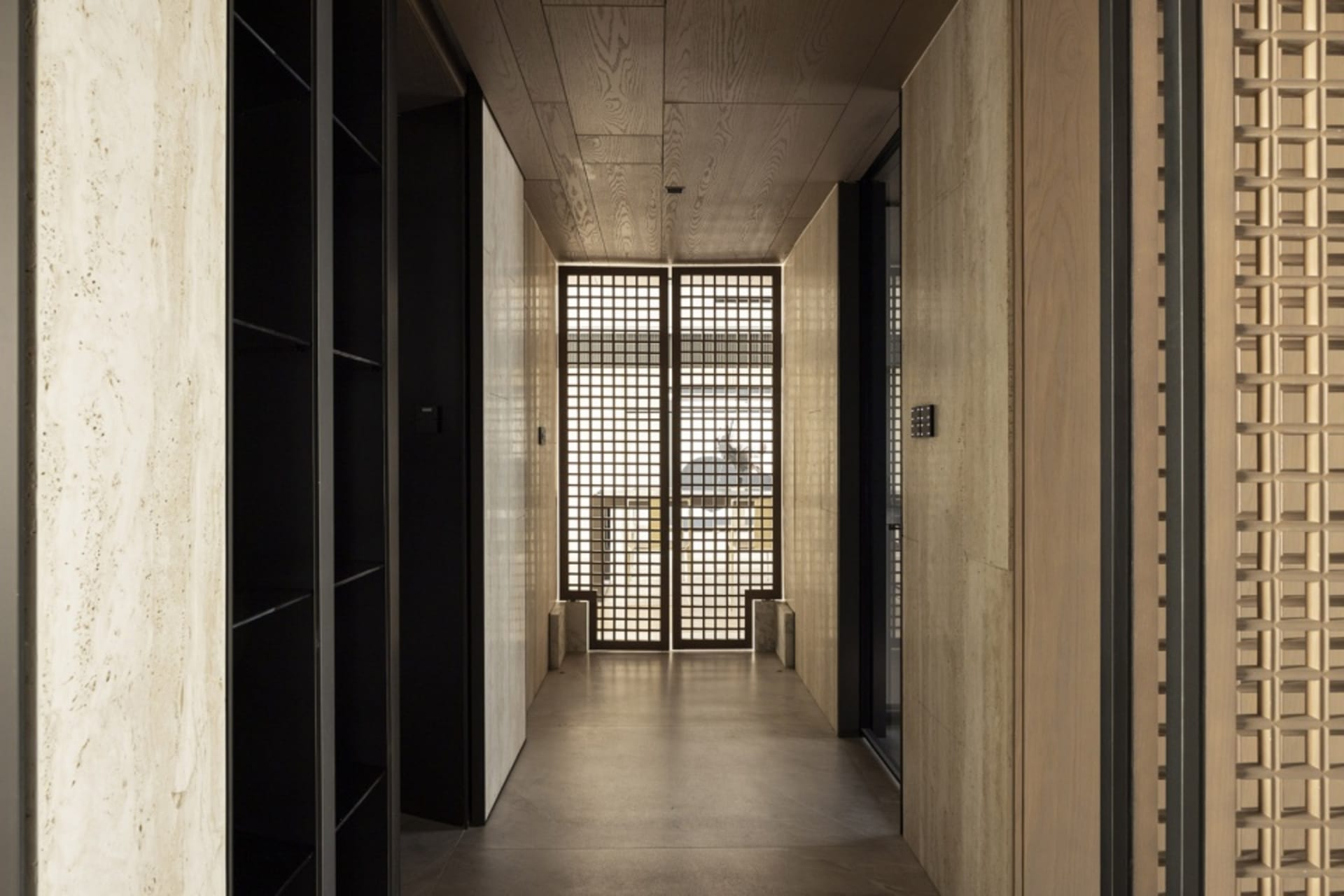 A minimalist corridor with wooden walls and a wooden ceiling, featuring a grid-patterned glass door.