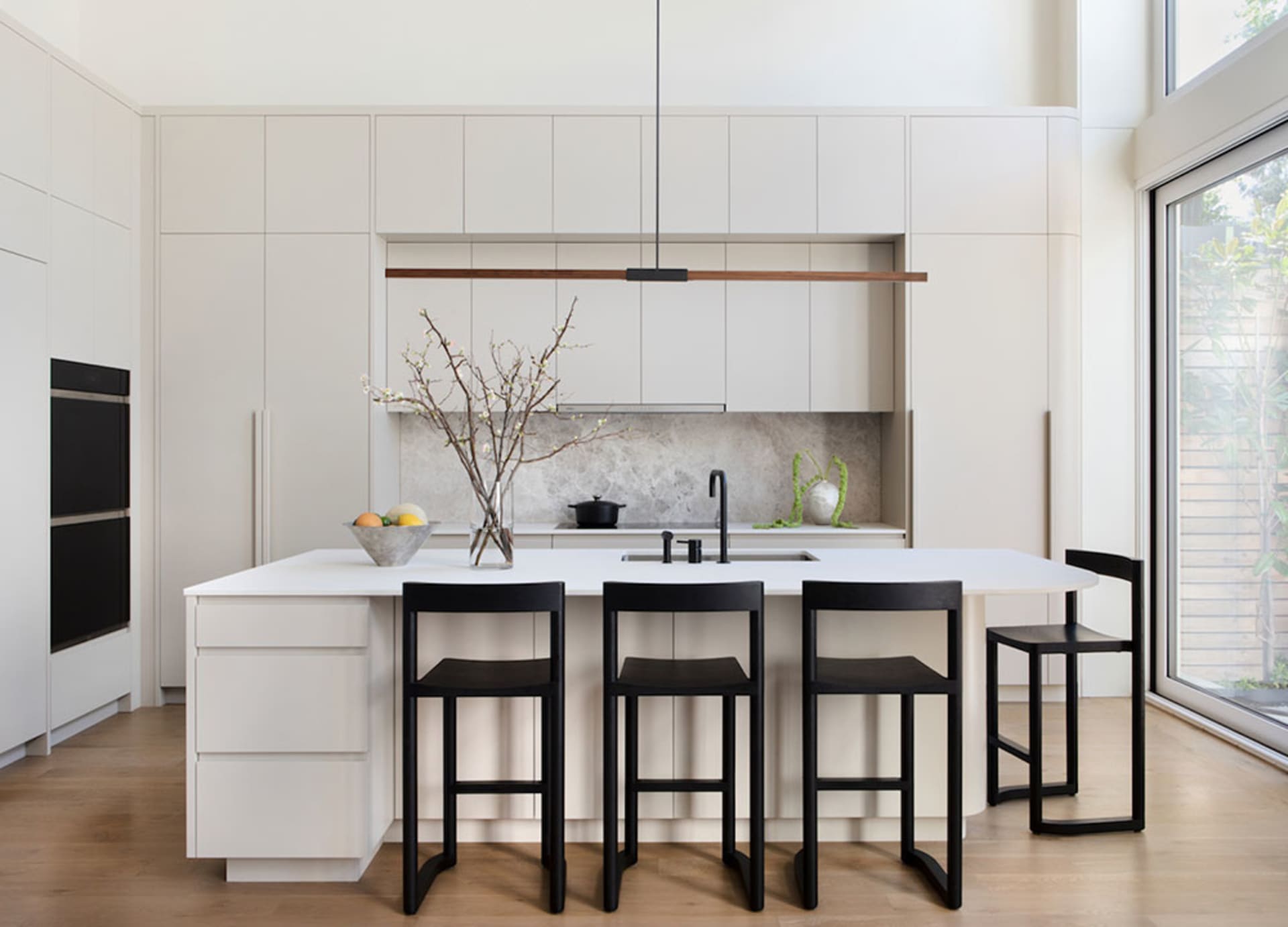 Modern minimalist kitchen with white cabinets, island, and black stools.