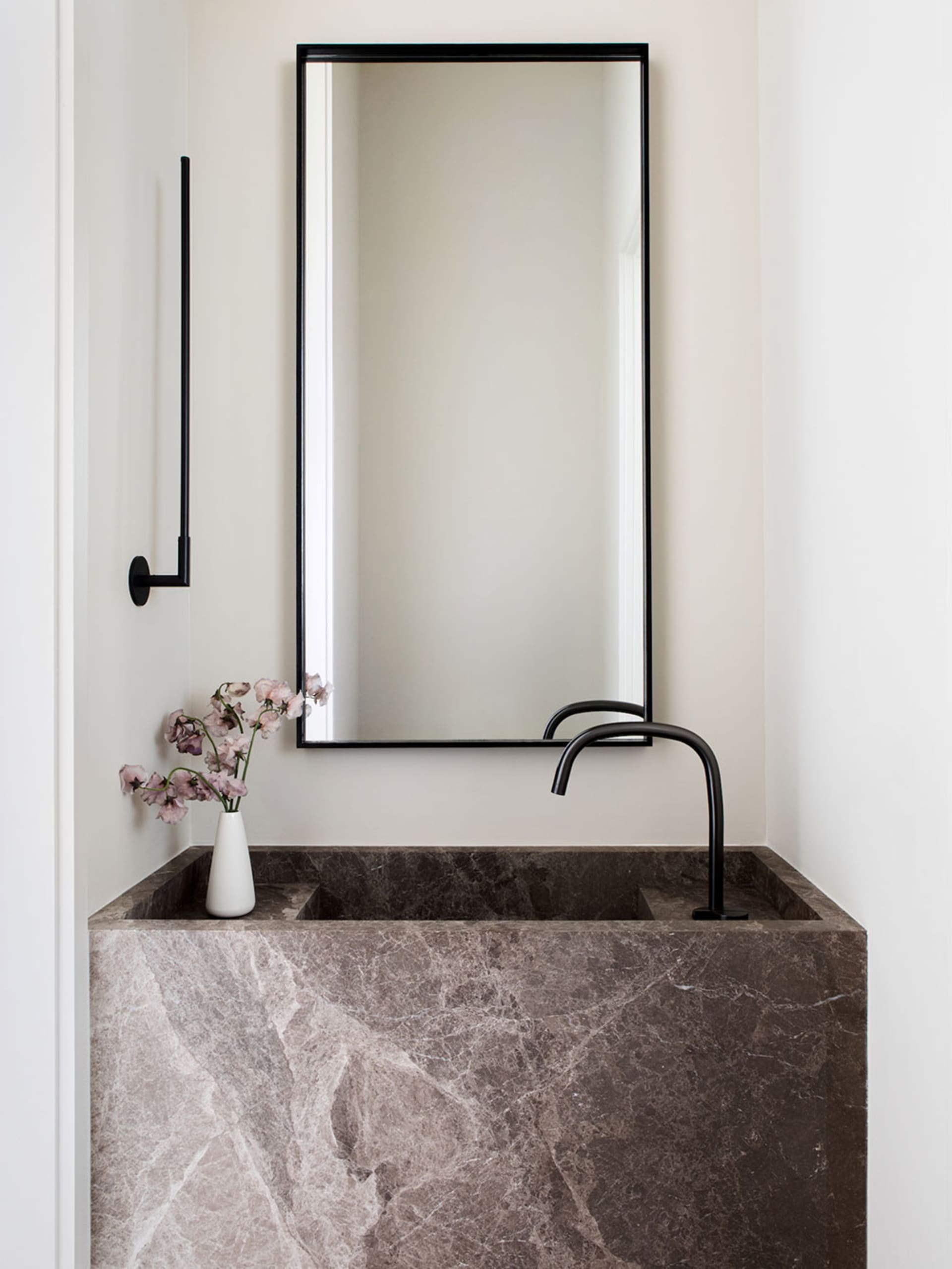 A modern minimalist bathroom featuring a marble sink, black faucet, and a vase of flowers on the counter.