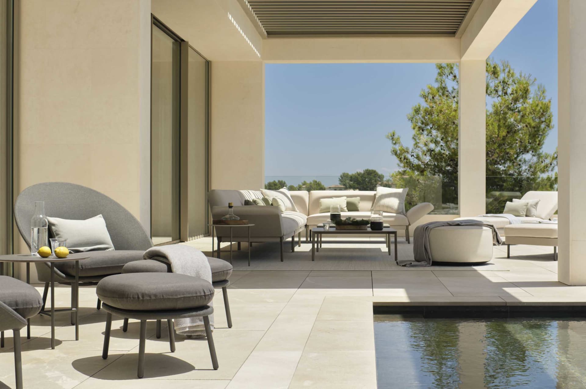 Modern patio featuring cement tiles with outdoor seating including sofas, ottomans, and tables, alongside a swimming pool wit