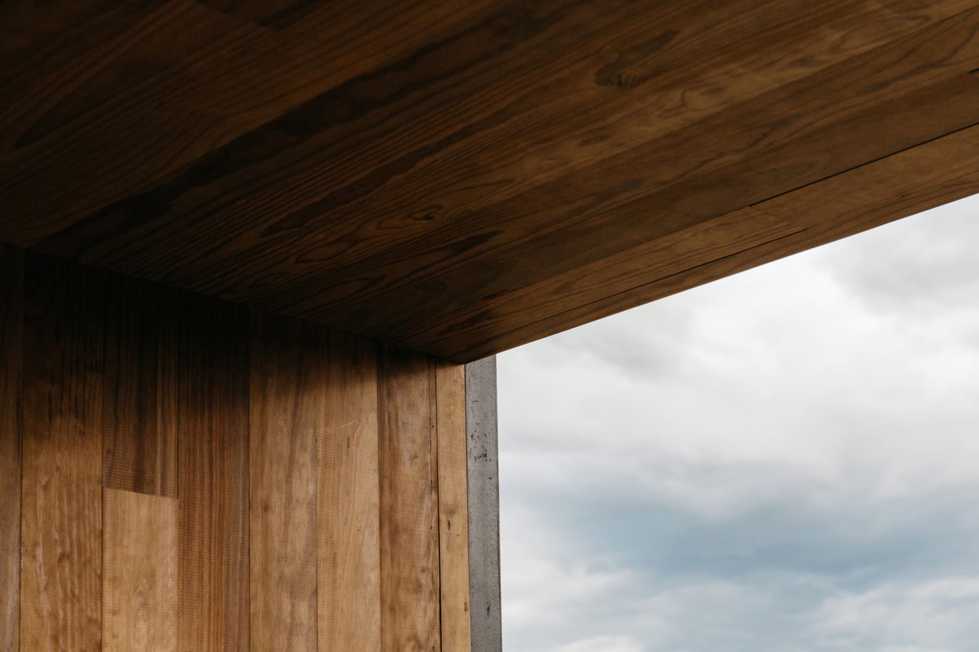 A modern window with a wooden ceiling and wall, against a cloudy sky.