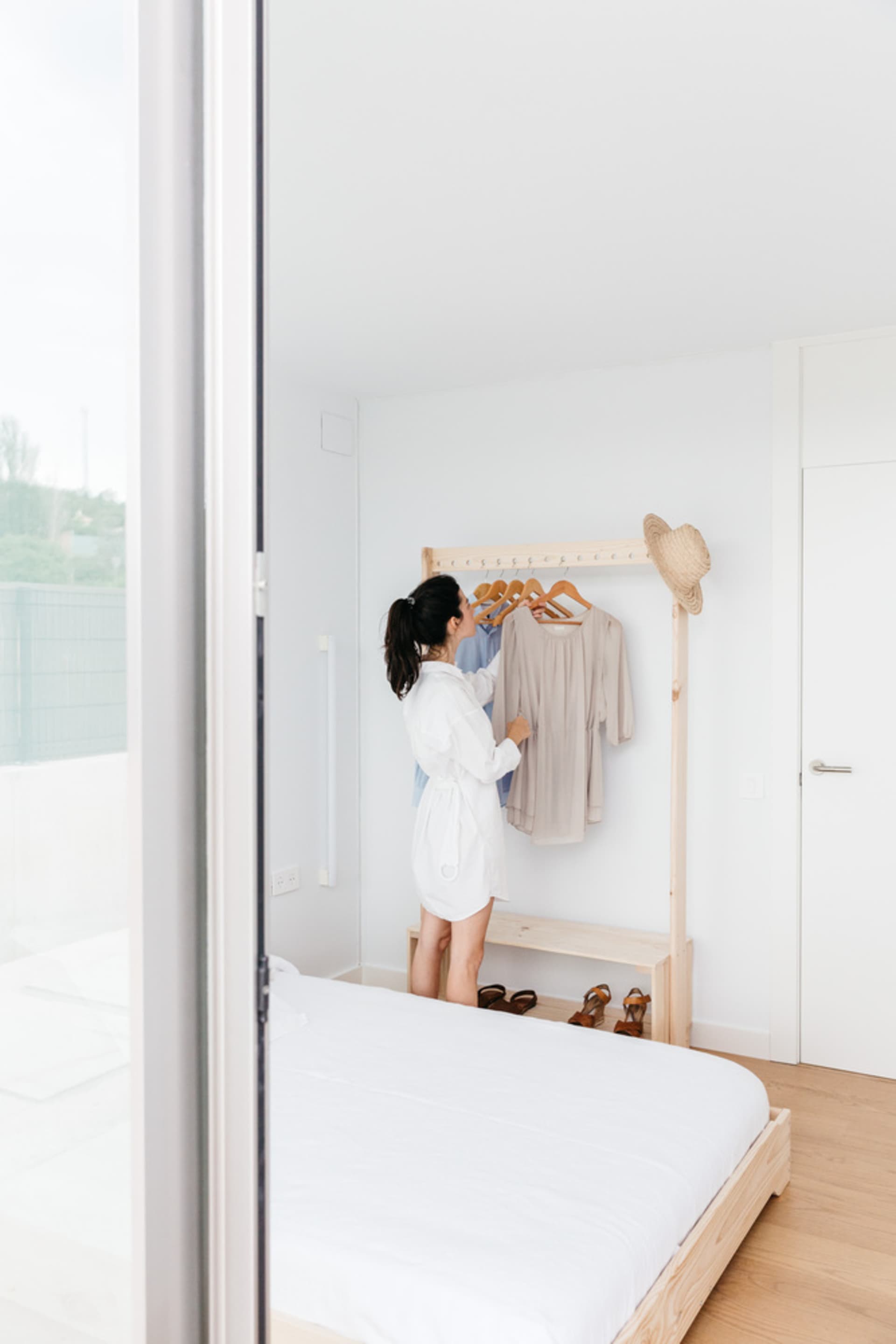 A minimalist bedroom featuring a wooden clothing rack with clothes hanging on it.