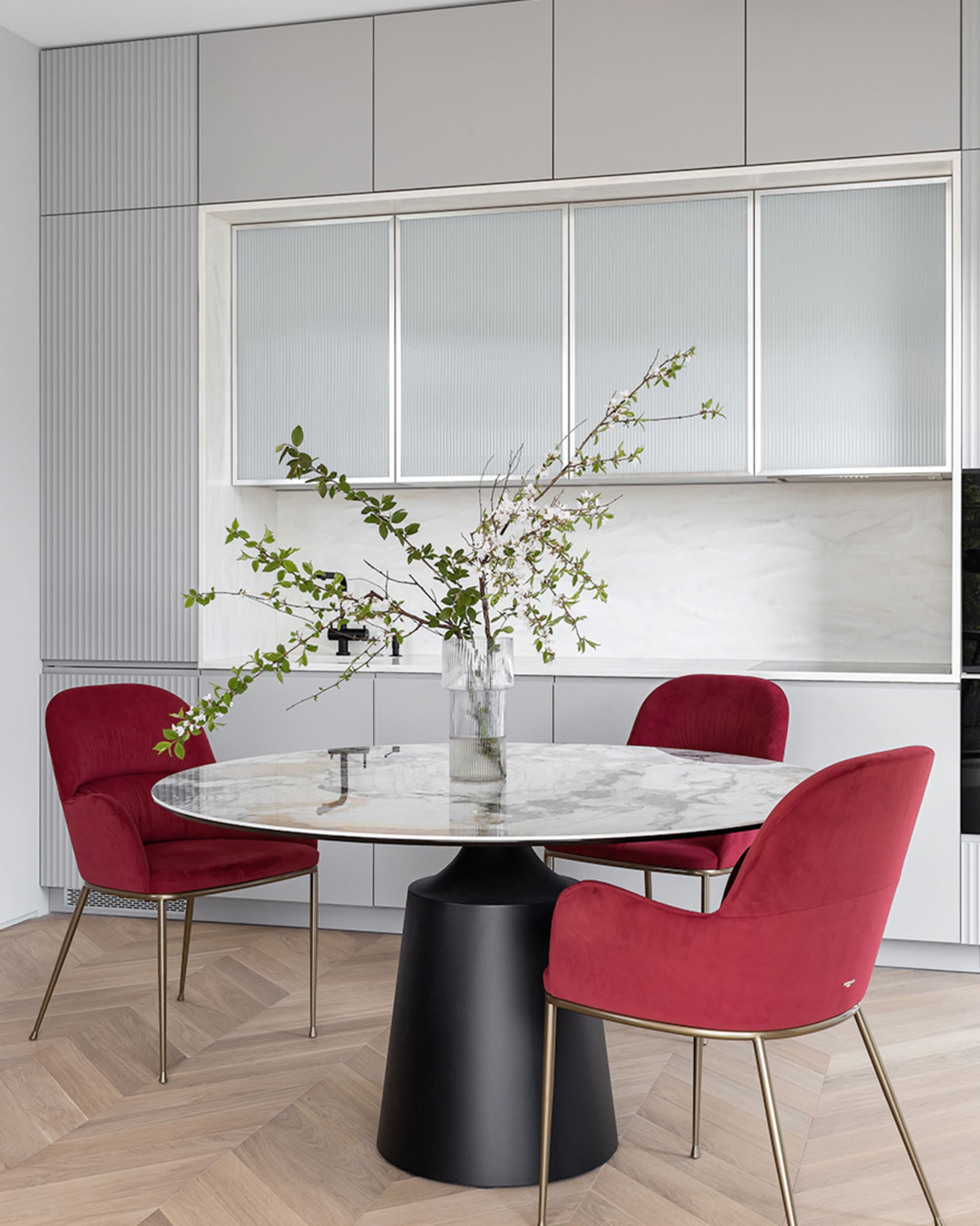 A modern dining room with a round marble table and red upholstered chairs.