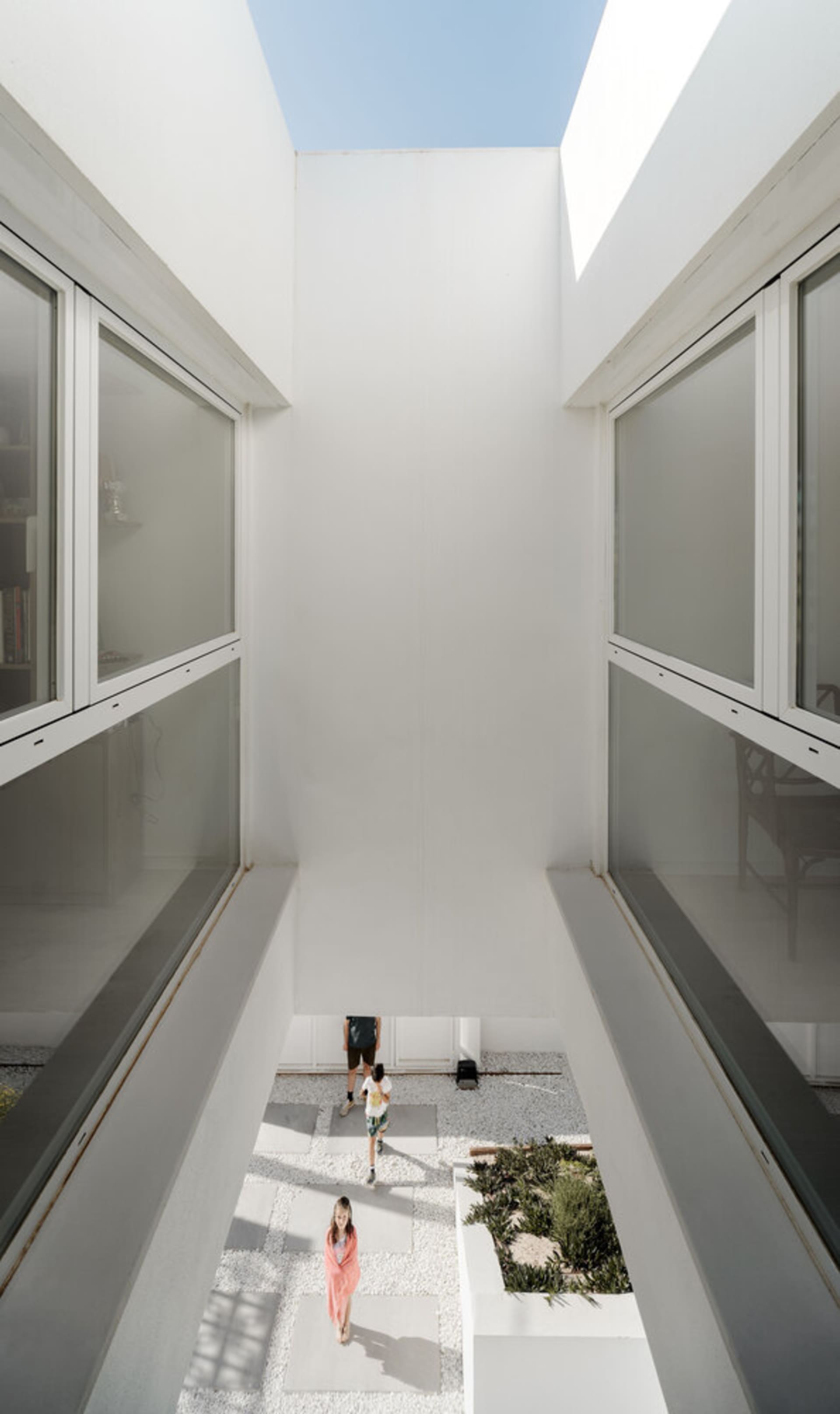 A modern house with a minimalist design featuring a central courtyard made of white concrete tiles, surrounded by clear glass