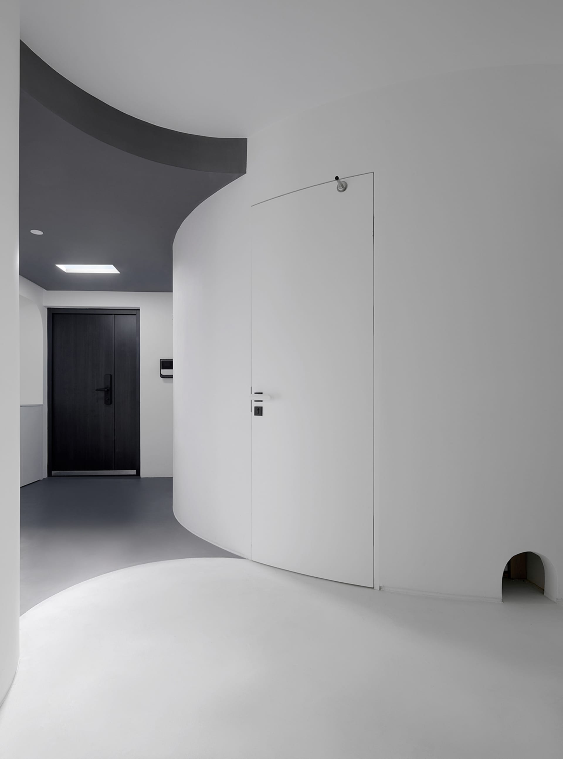 A modern entrance featuring a curved concrete wall and a black door.