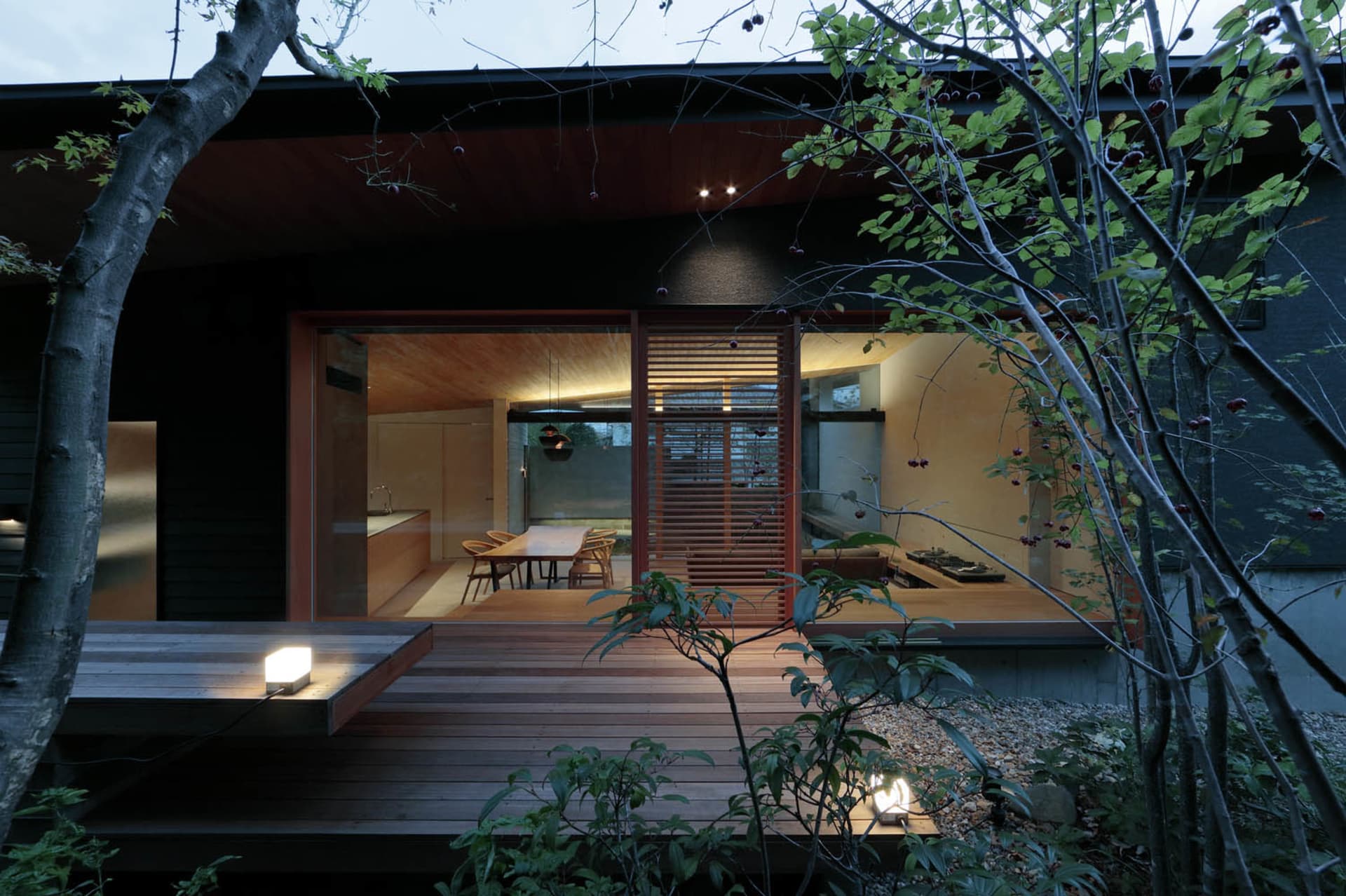 A modern house exterior with wooden planks and illuminated windows.