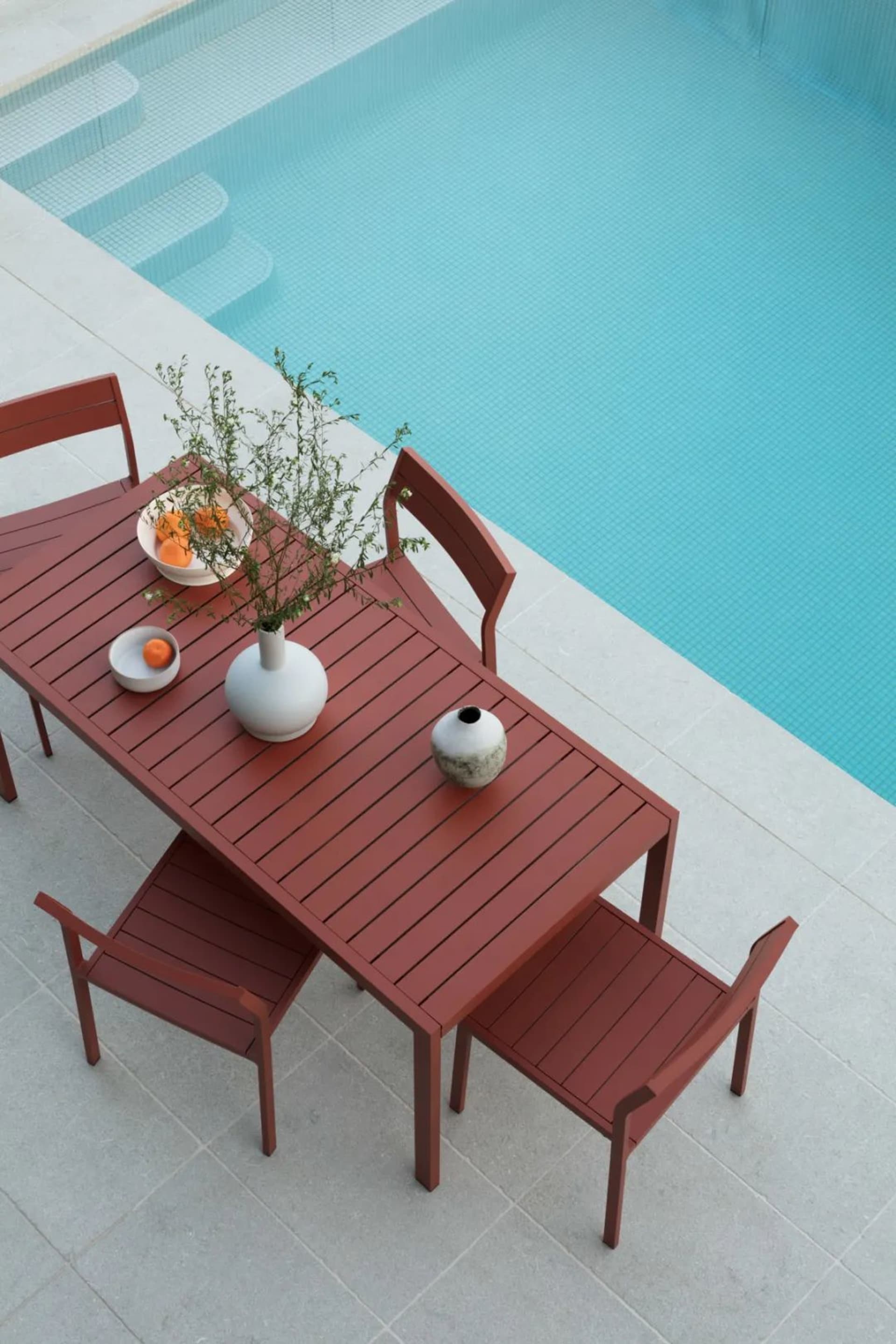 Modern outdoor patio furniture with metal table and chairs featuring plant and orange bowl.