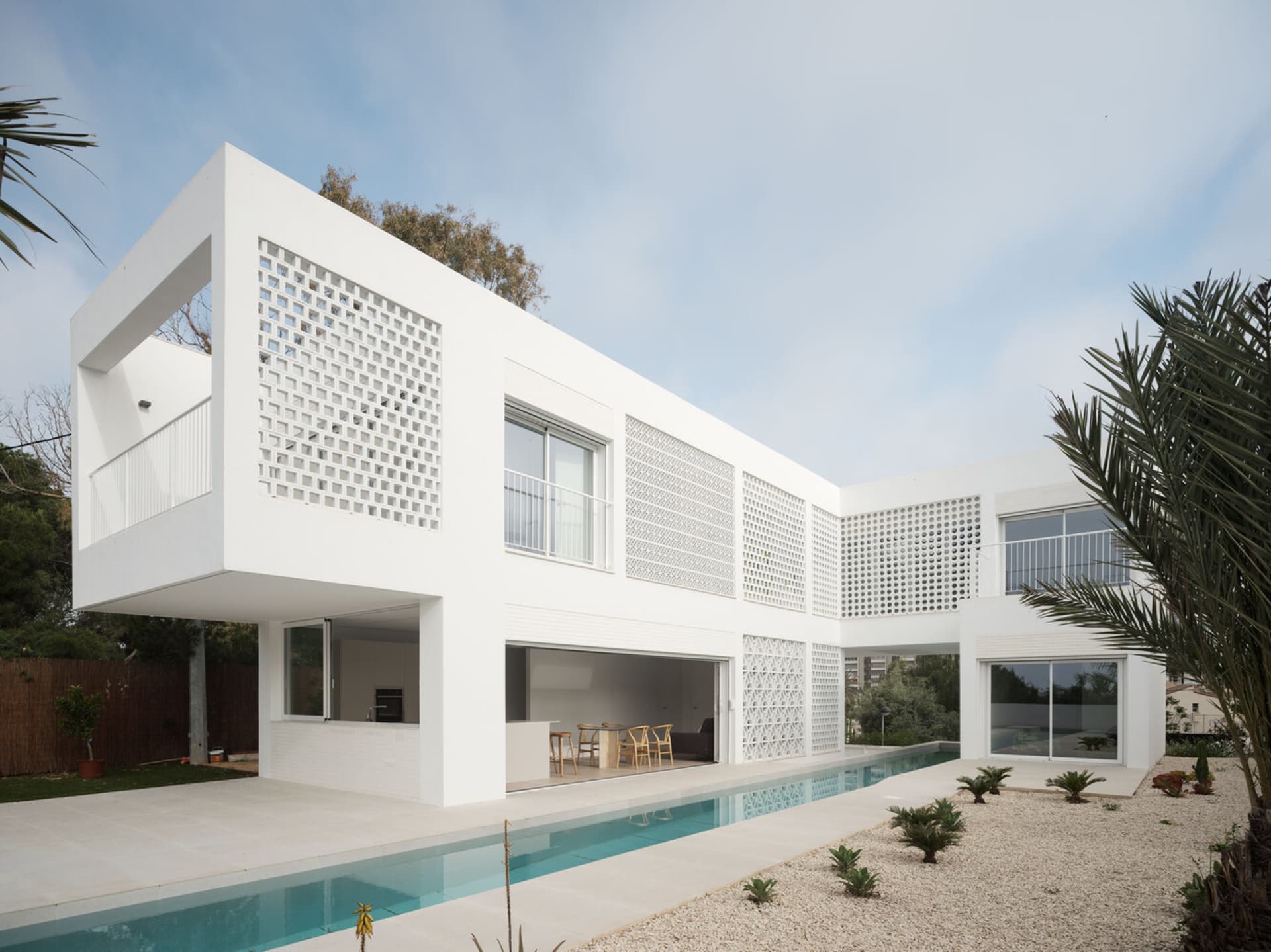 A minimalist modern house with a white concrete exterior, featuring a balcony and a swimming pool.