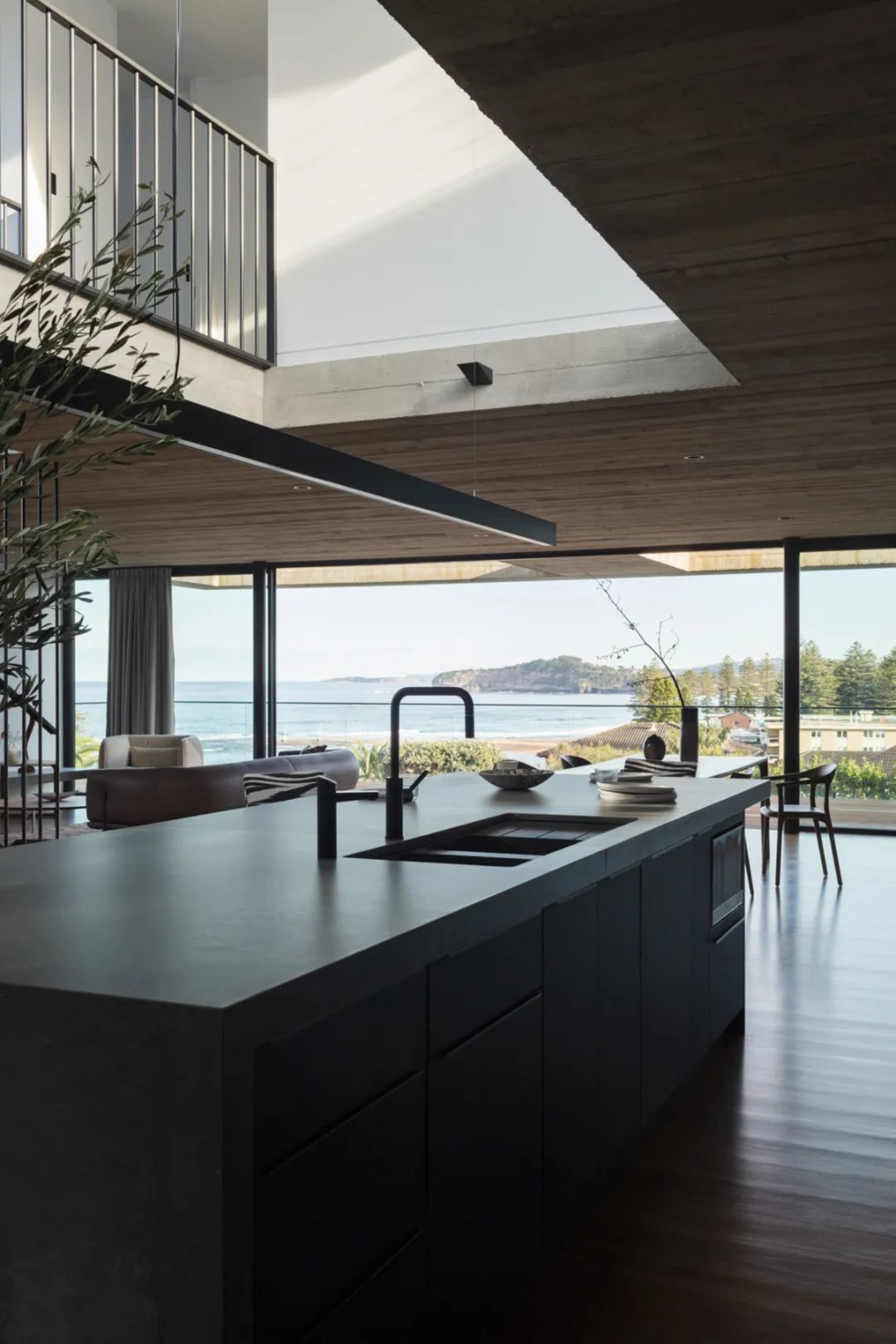 Contemporary kitchen with concrete and glass materials, featuring an island with a sink and a view of the ocean.