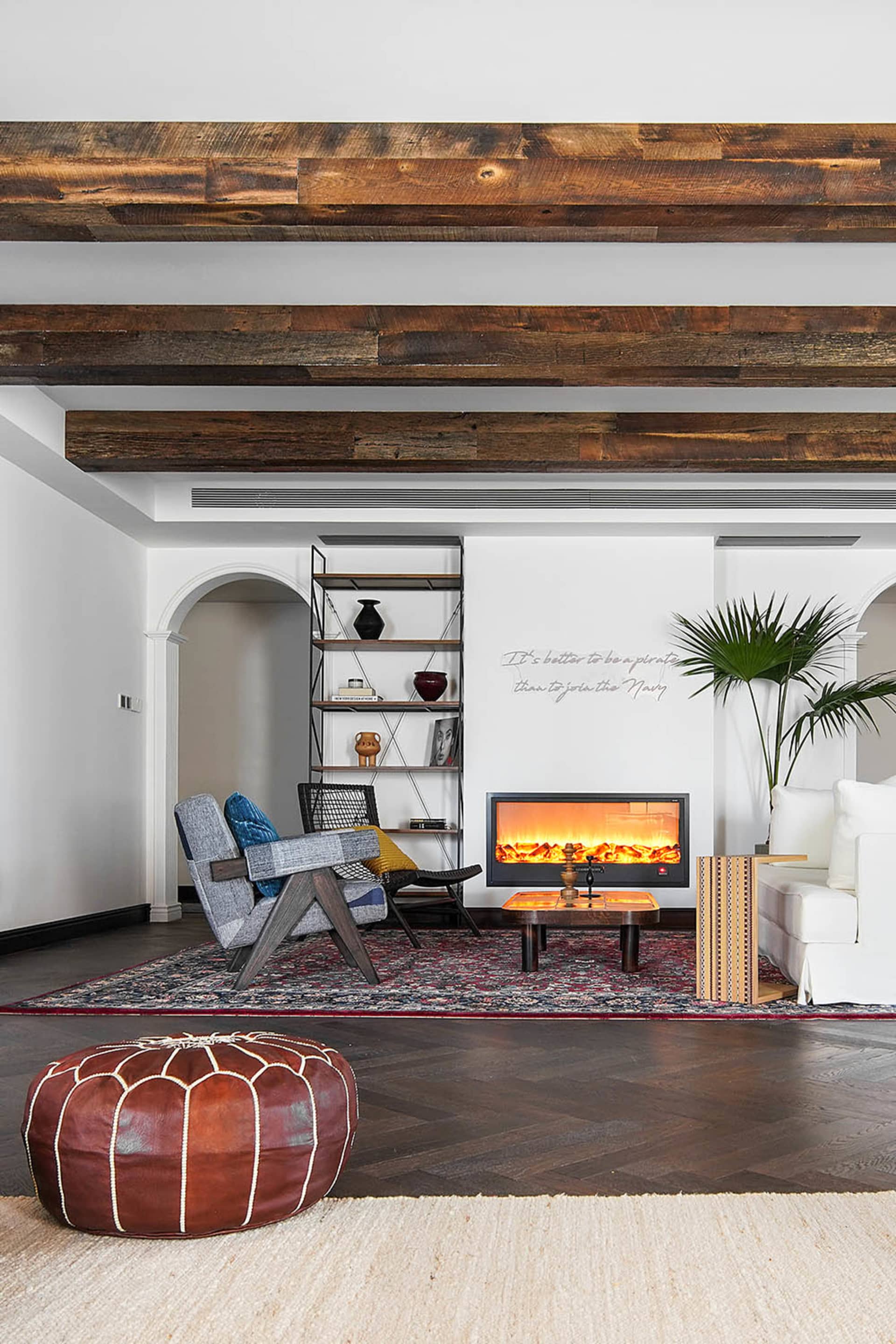 A cozy industrial-style living room with wood beams, a warm fireplace, and a mix of vintage and modern furniture.