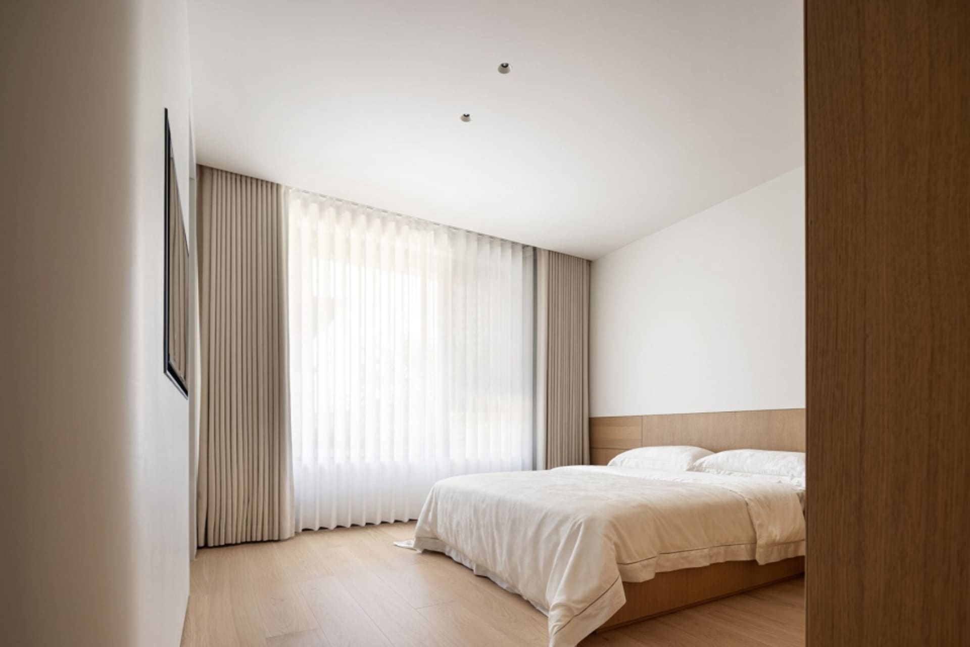 Minimalist bedroom with a bed, wooden furniture, light textiles, plastic blinds, white walls, and a wooden floor.