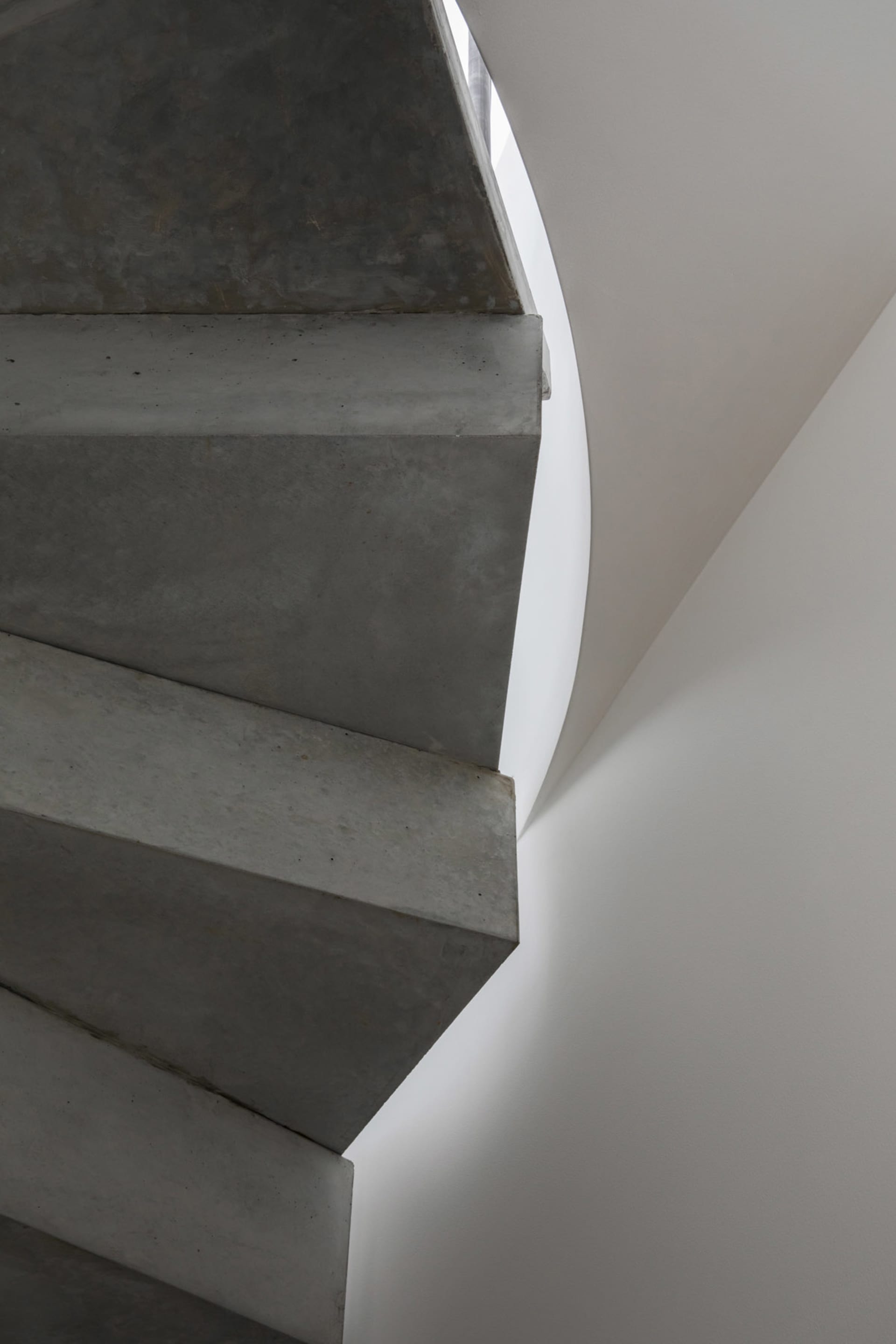 A sleek, modern concrete staircase with a curved wall and white ceiling in an interior setting.