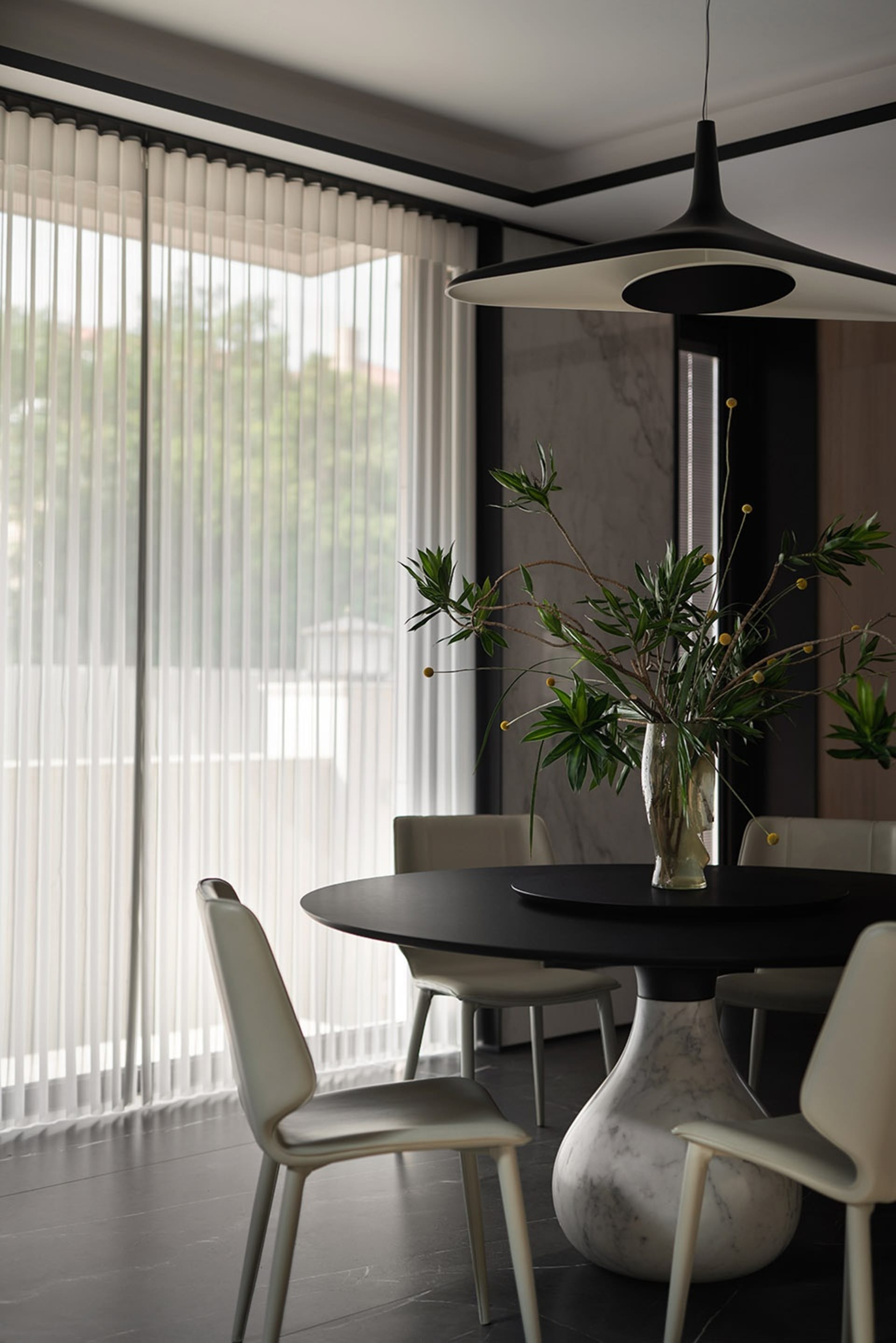 A modern dining room featuring a round black marble table and sleek white chairs under a contemporary pendant light.