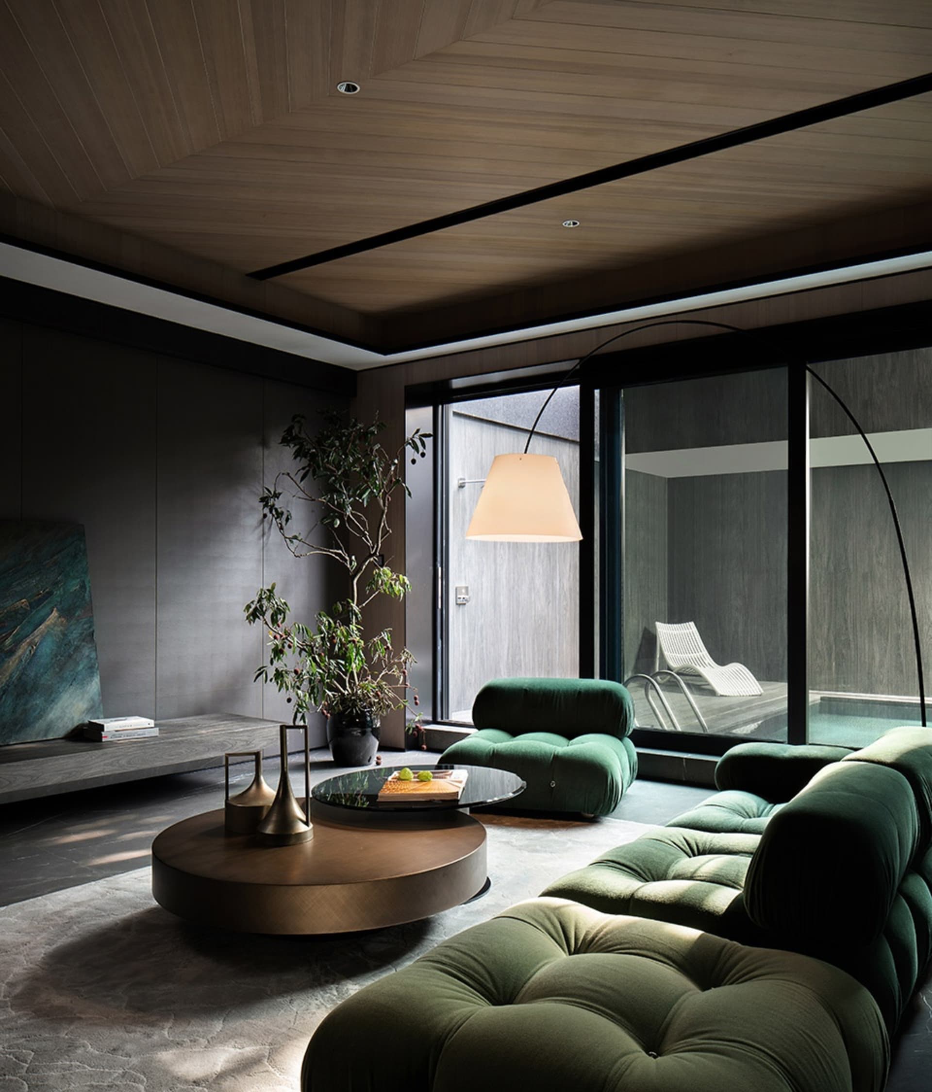 A modern living room with green upholstery, wooden ceiling, and glass wall.