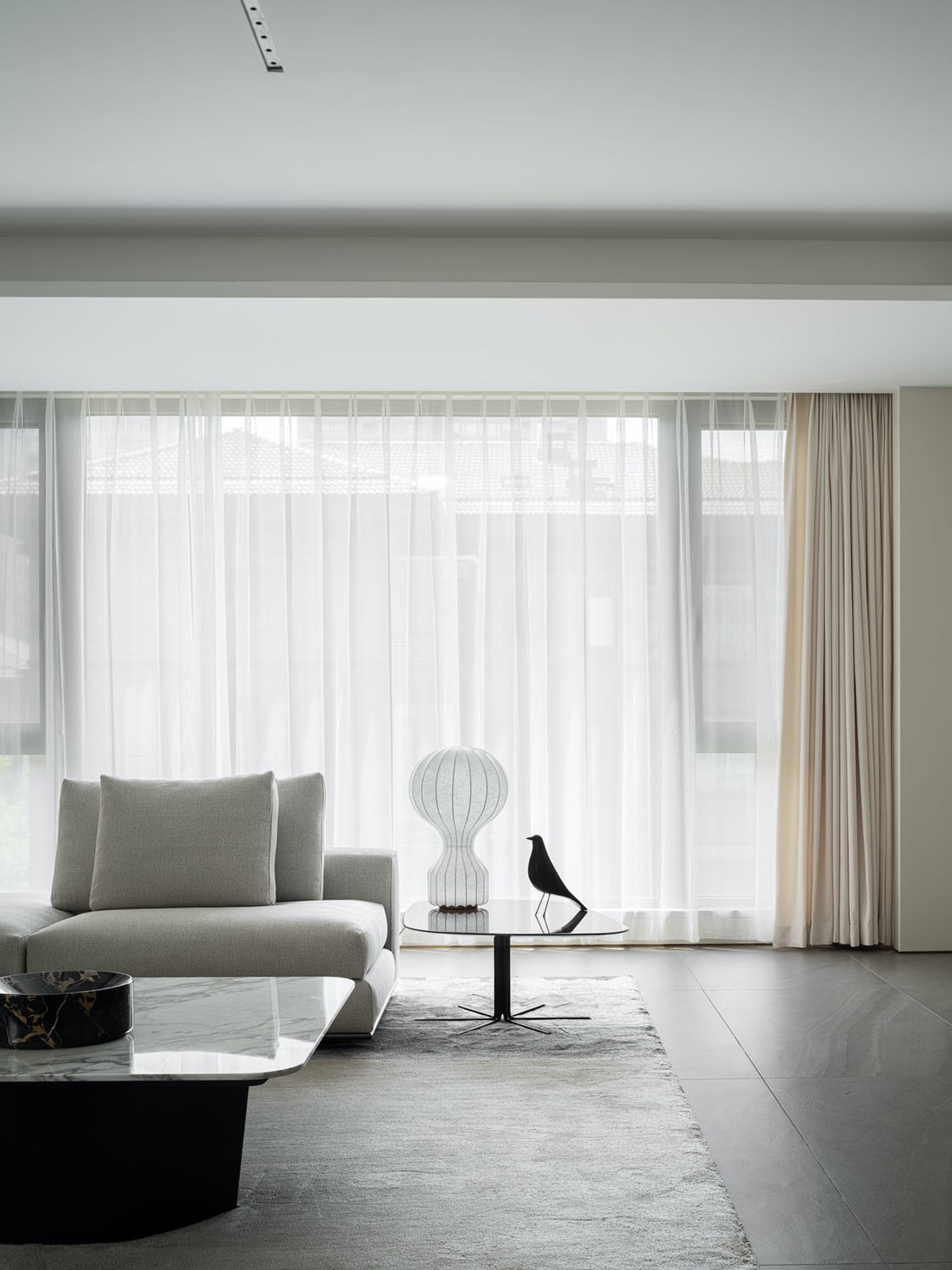 Modern living room featuring a glass coffee table, a stone floor, and white sheer curtains.