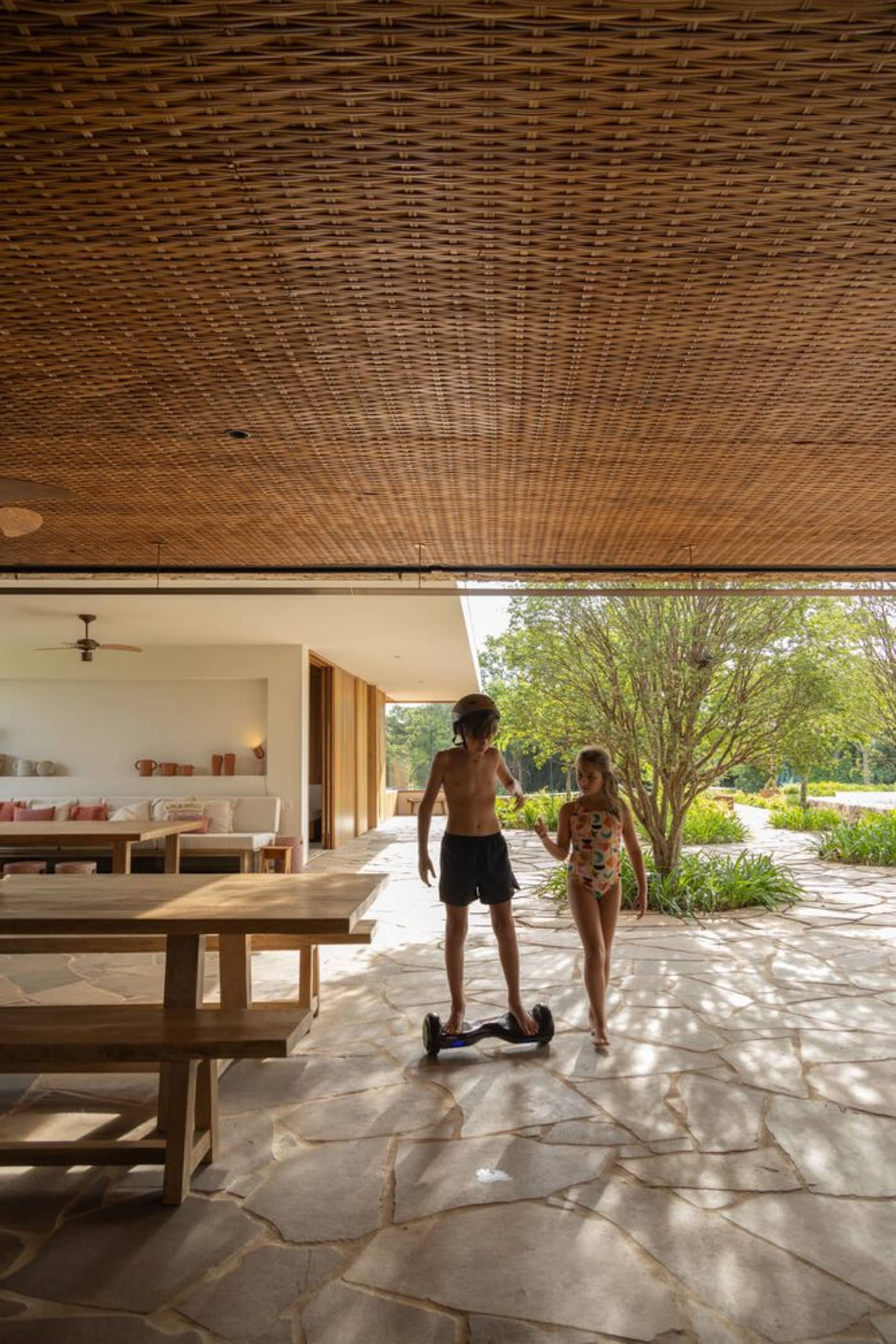 Children playing with a hoverboard in a modern residential interior with a woven wood ceiling and wooden furniture and floors