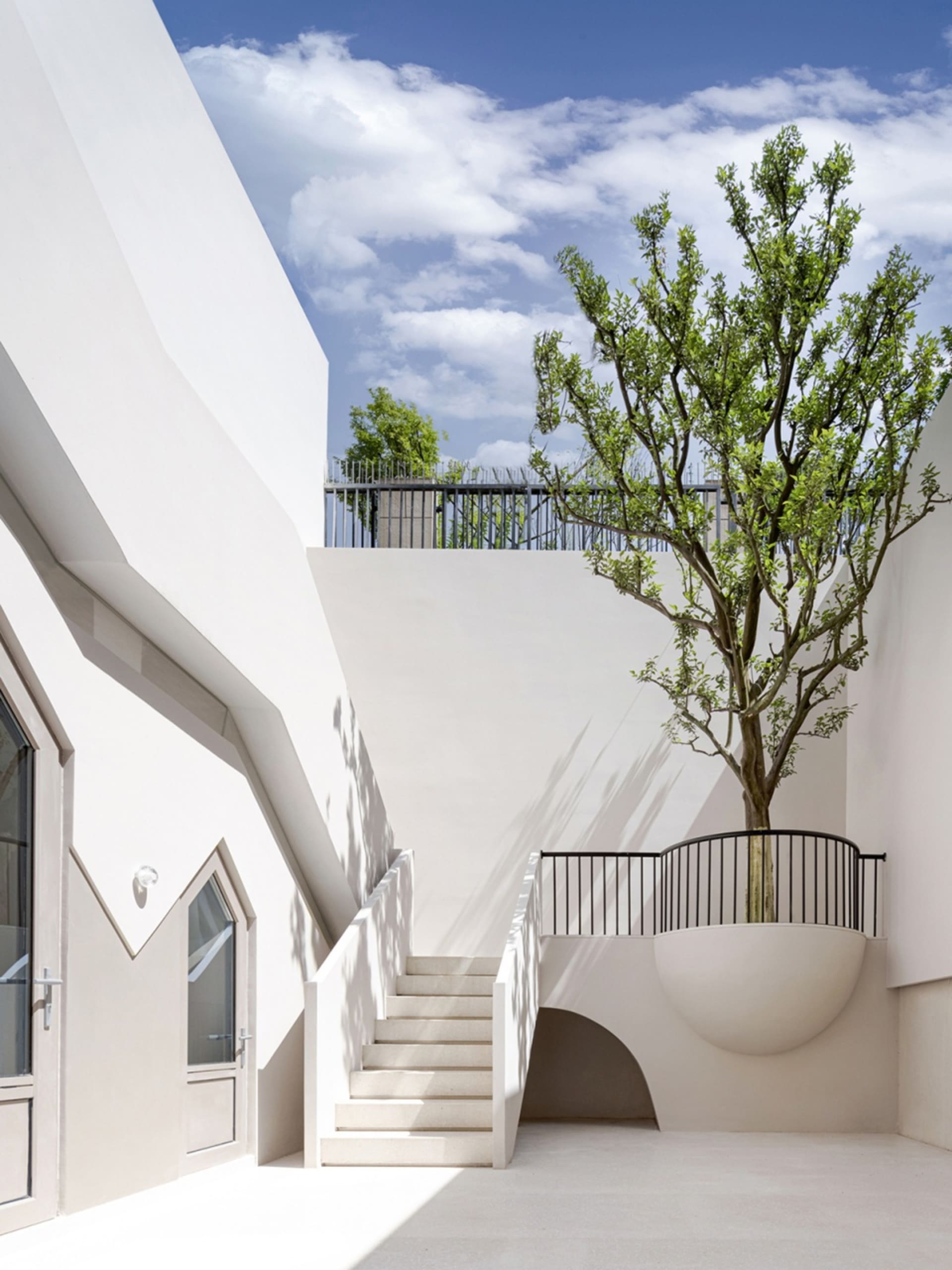 Modern white building with a concrete staircase and tree in a planter.